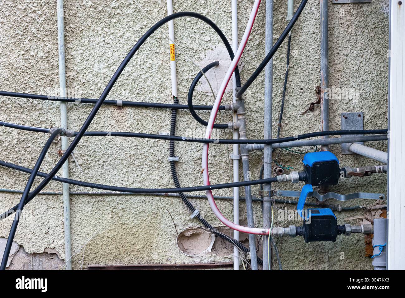 Vieux tuyaux d'alimentation en eau avec vannes et compteurs montés sur le mur extérieur d'un bâtiment résidentiel. Infrastructure urbaine et système de distribution d'eau con Banque D'Images