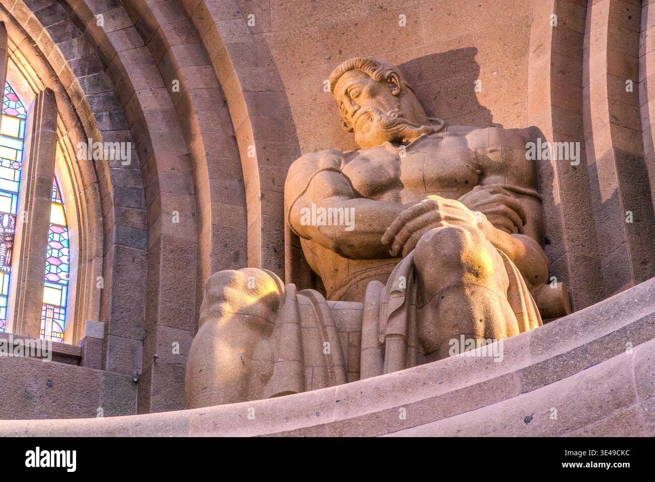 La crypte du Monument à la bataille des Nations : l'une des quatre figures gardiennes monumentales (le guerrier en deuil) dans sa niche avec des vitraux colorés ; vue en bas angle. Leipzig, Saxe, Allemagne Banque D'Images