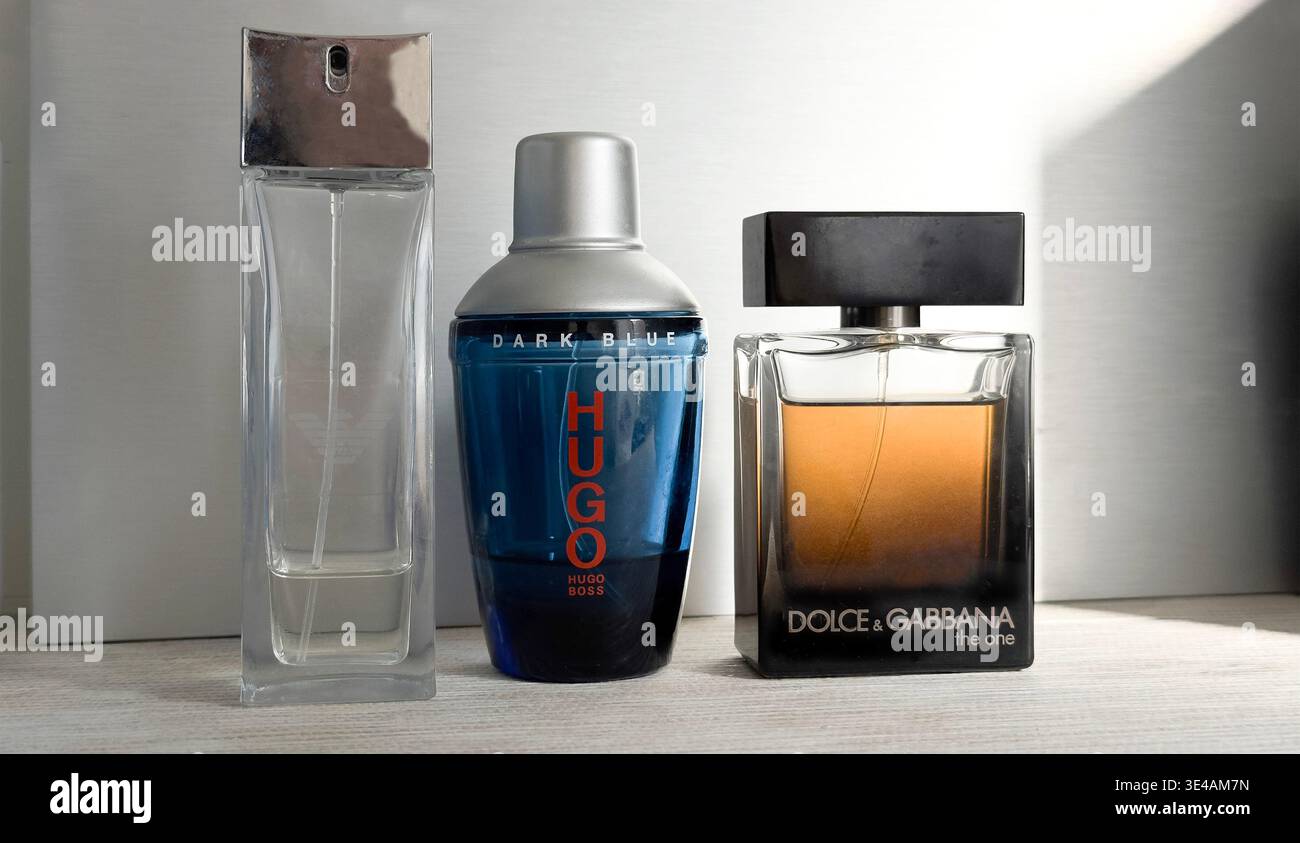 Trois bouteilles de parfum design pour homme après rasage, dont Hugo Boss, Dolce & Gabbana & Georgio Armani placées sur une surface en bois avec lumière de fenêtre - Image de stock capturée avec un smartphone