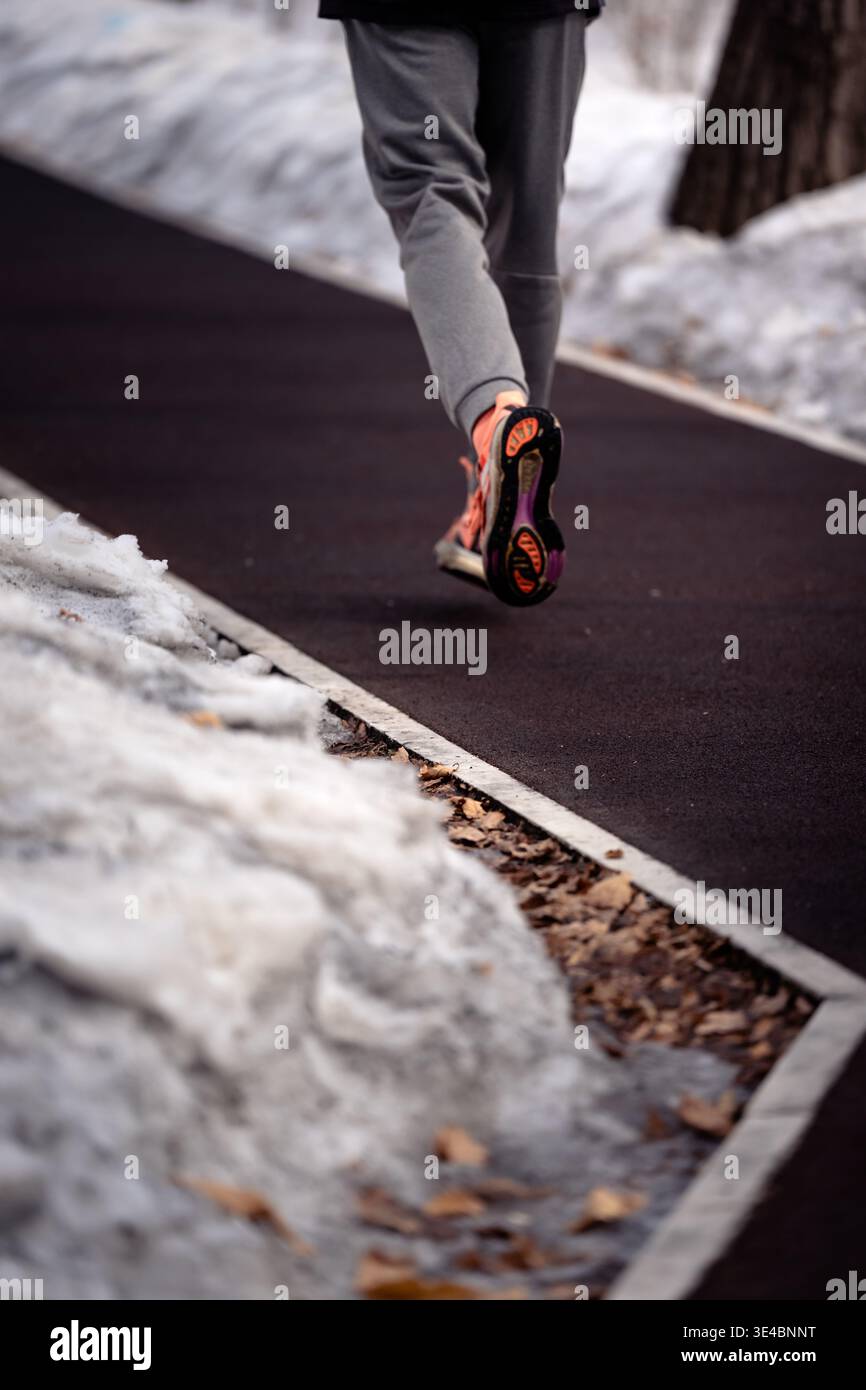 Un coureur en tenue athlétique brillante fait du jogging le long d'un chemin dégagé entouré de neige hivernale Banque D'Images