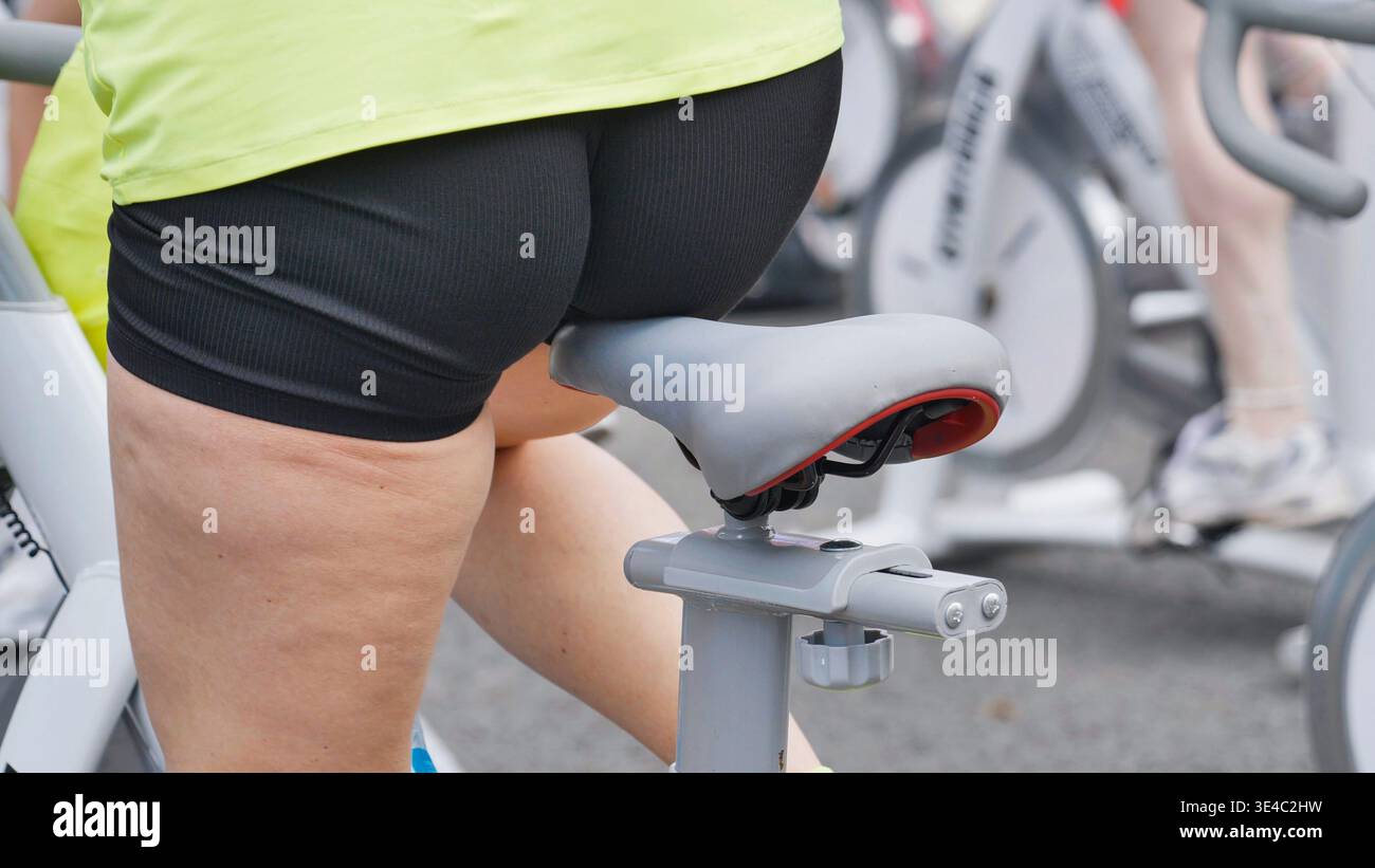 Gros plan du bas du corps d'une femme en surpoids sur un vélo d'exercice au gymnase. Banque D'Images