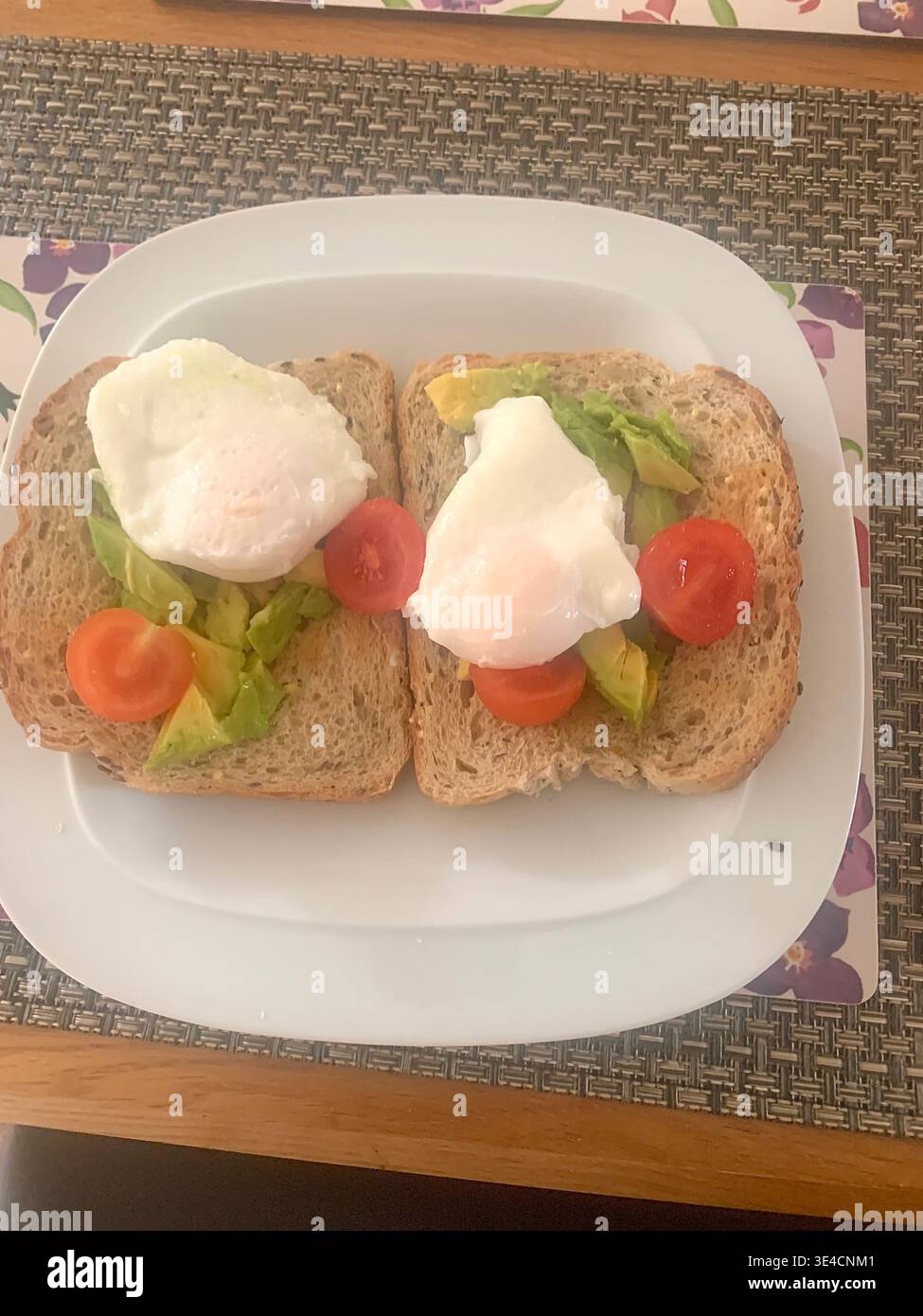 Une assiette de petit déjeuner saine avec pain grillé à l'avocat aux grains entiers garni d'œufs pochés et de tomates cerises servie sur un napperon tissé en Angleterre au Royaume-Uni - Image de stock capturée avec un smartphone