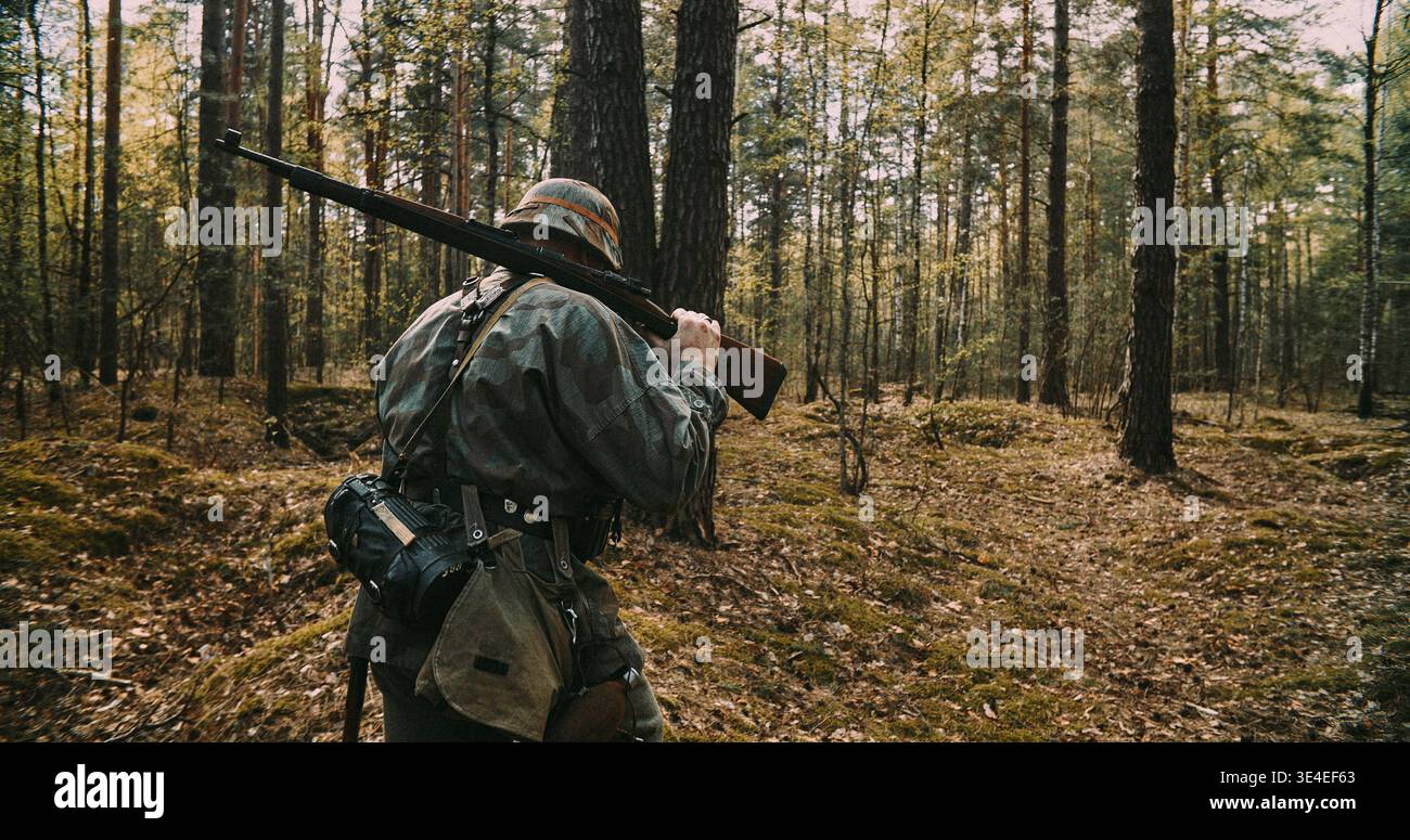 Vue arrière d'un soldat allemand marchant dans la forêt avec un fusil pendant la seconde Guerre mondiale Banque D'Images