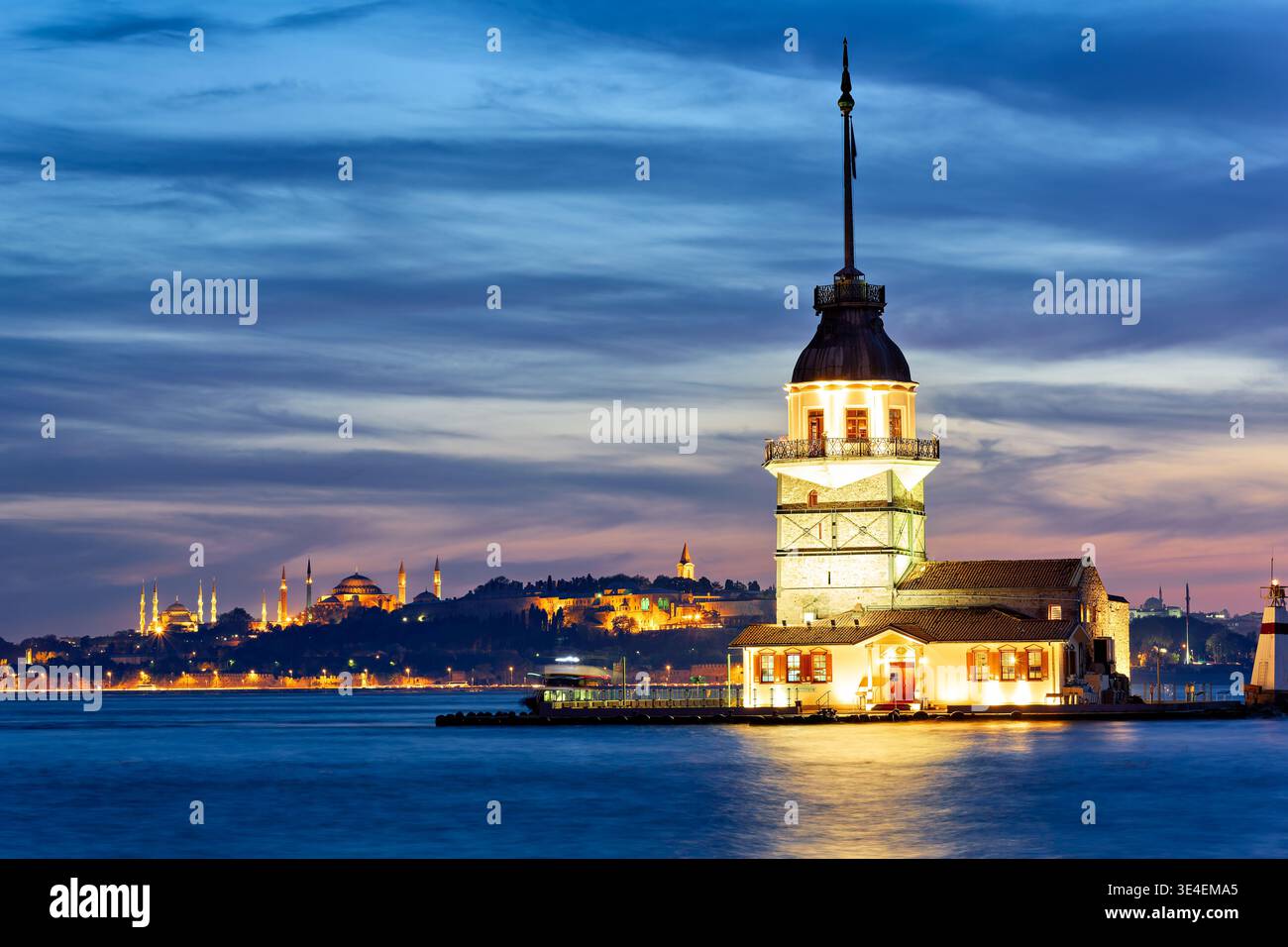 Maiden's Tower se dresse sur le Bosphore alors que le soleil se couche derrière les gratte-ciel d'Istanbul. Les lumières scintillent alors que le jour se transforme en nuit. Banque D'Images