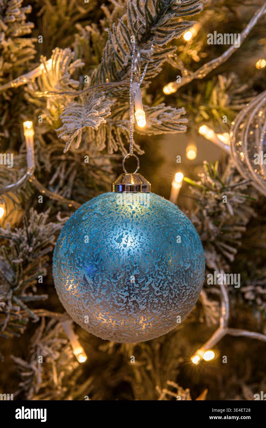 Boule de Noël bleue suspendue à un arbre décoré avec des lumières de fée blanches chaudes et des branches givrées Banque D'Images