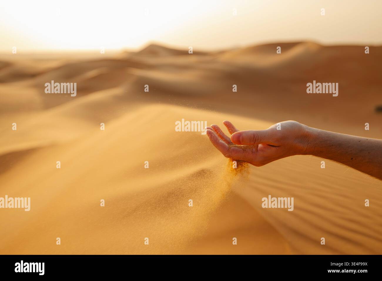Gros plan de la main laissant couler le sable dans le vent dans le désert d'Abu Dhabi, eau. Textures désertiques, éléments naturels, voyages, aventures et paysages du moyen-Orient c Banque D'Images