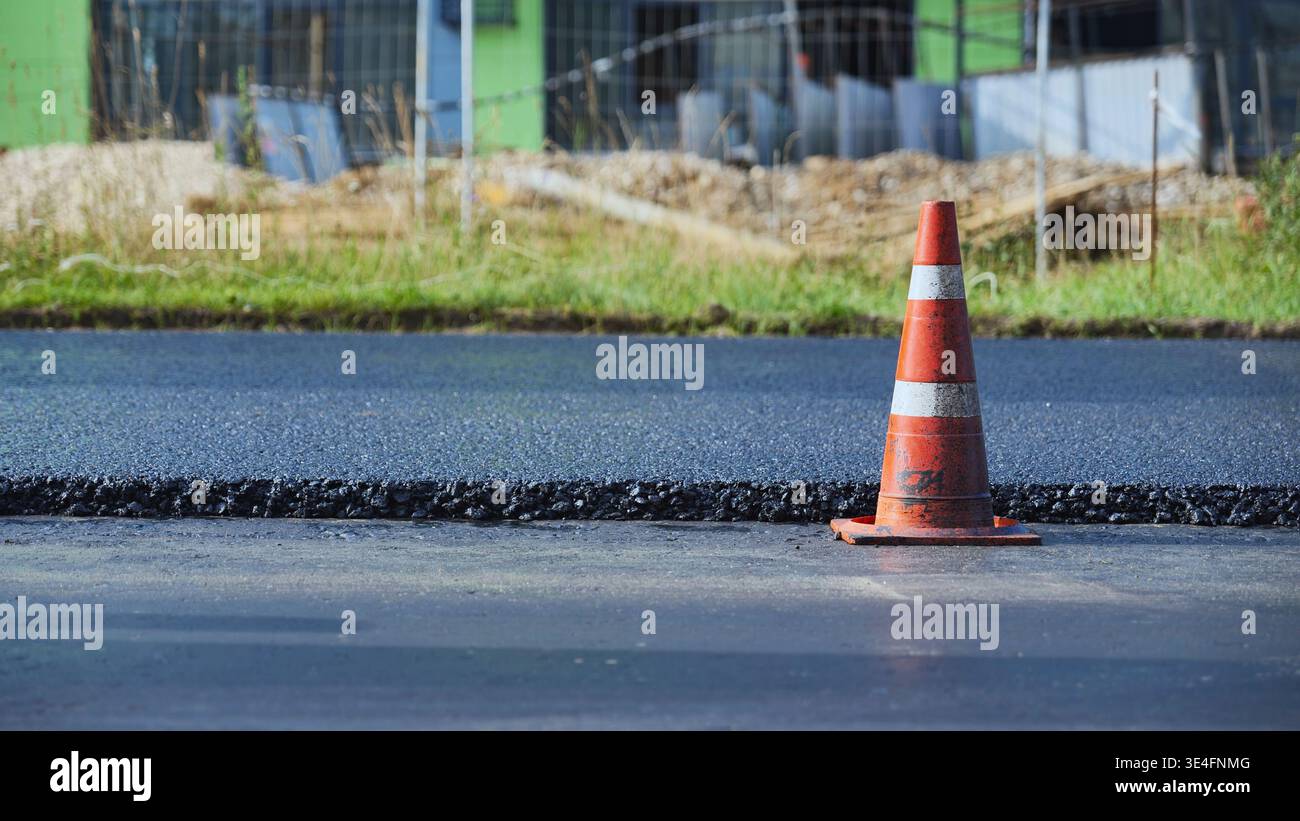 Cône de circulation orange marquant une nouvelle rue asphaltée pendant les travaux routiers d'infrastructure Banque D'Images