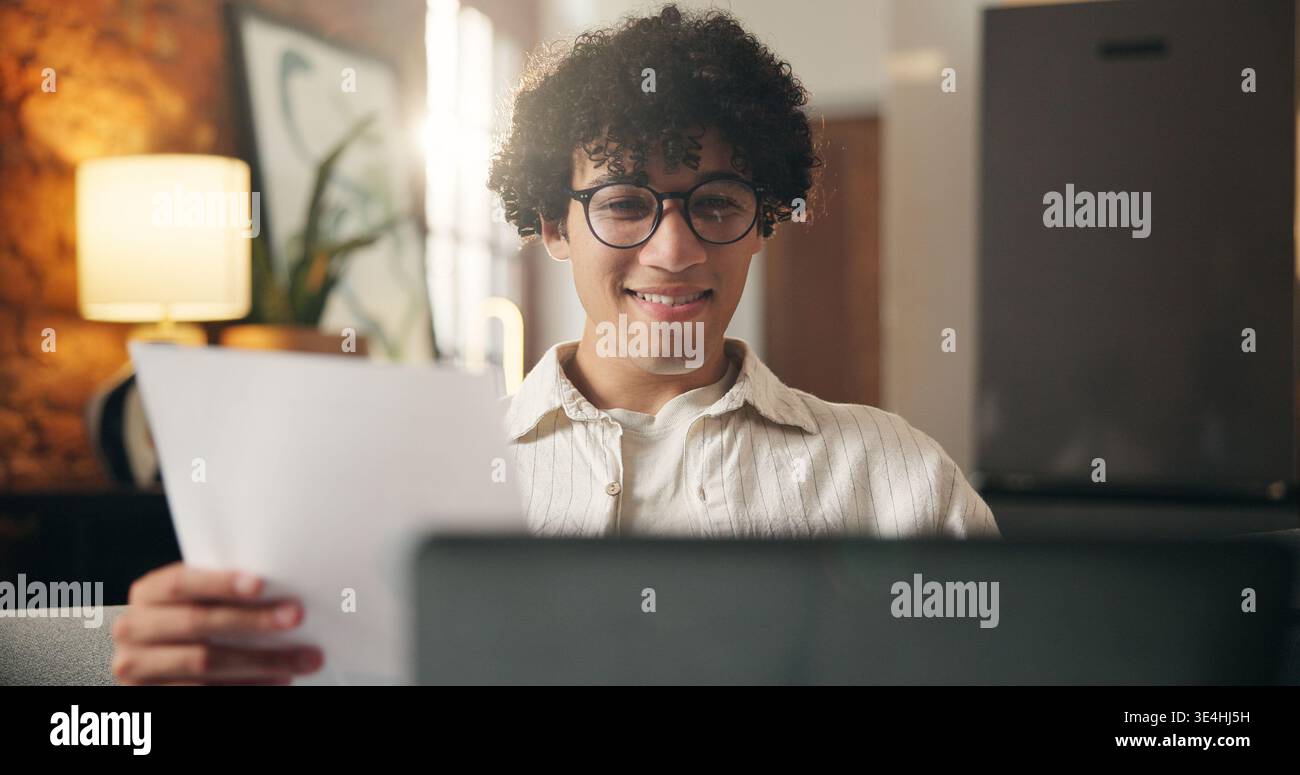 Homme, document et ordinateur portable dans la maison avec travail à distance, lunettes et vérification de journaliste pour l'histoire. Auteur freelance, personne et relecture à la maison Banque D'Images