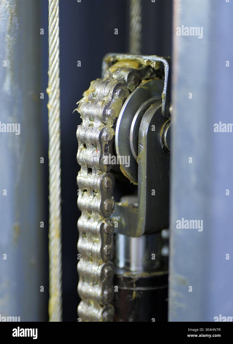 Un gros plan d'un mécanisme de levage de voiture extra-robuste montre une chaîne à feuilles lubrifiée, une poulie et un câble en acier avec des composants hydrauliques dans un kit d'atelier Banque D'Images