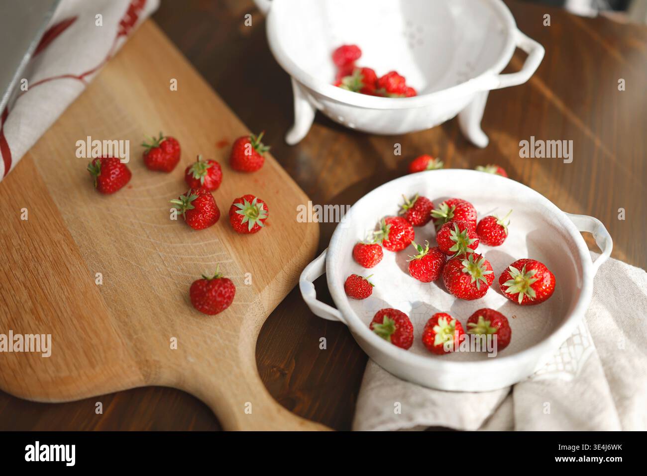 Fraises biologiques fraîches sur planche de bois et bols en céramique vintage. Scène de cuisine rustique à la mode avec baies rouges, passoire blanche et lumière du soleil Banque D'Images