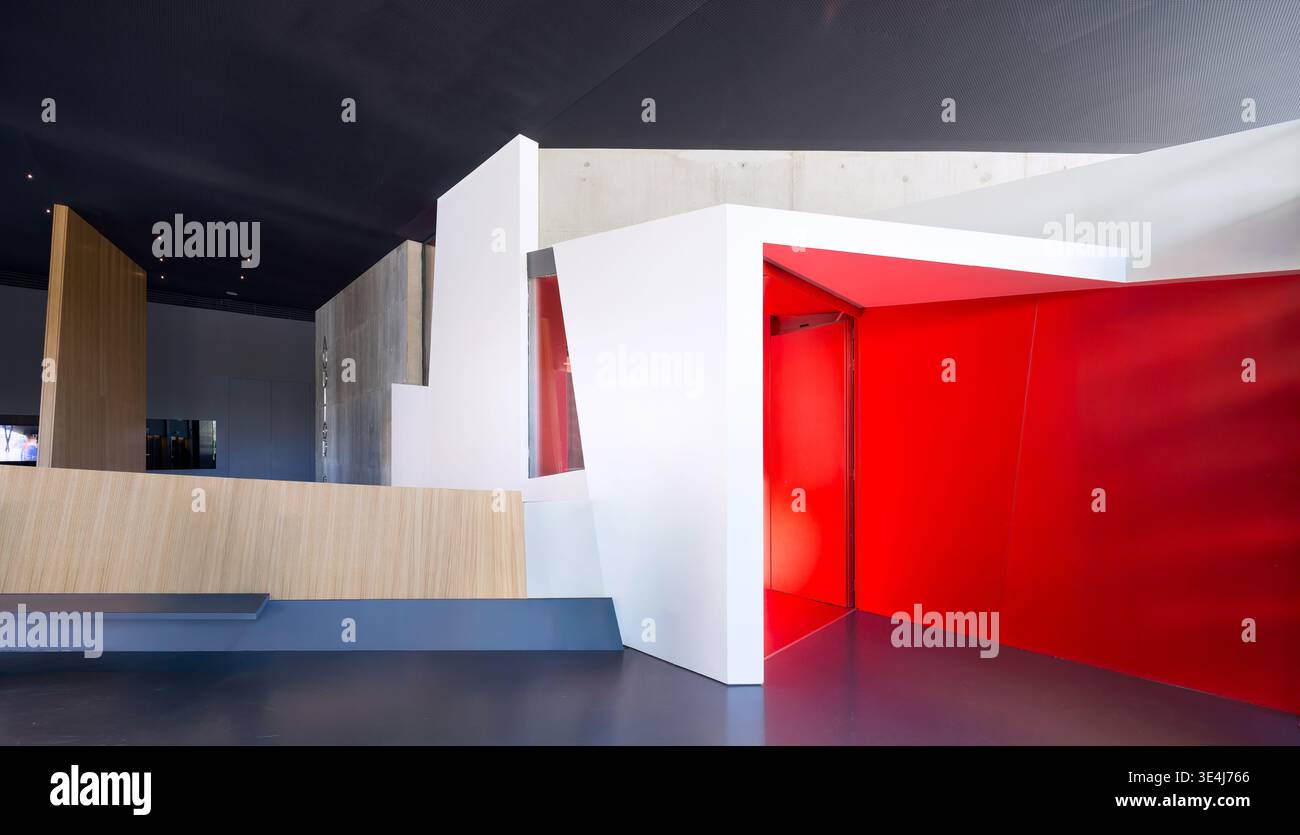 Une salle d'exposition contemporaine à l'architecture élégante et angulaire mise en valeur par des éléments rouges vifs et blancs immaculés, offrant un art dynamique Banque D'Images