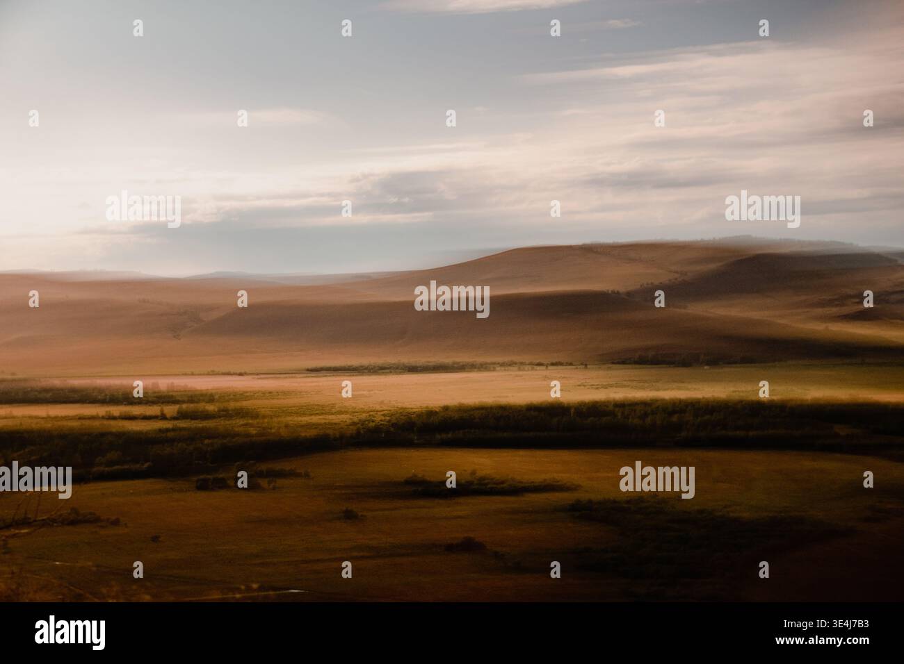 Prairie dorée au coucher du soleil avec des collines ondoyantes et des prairies ouvertes sous des nuages doux, capturé avec un flou de mouvement subtil pour une atmosphère rêveuse et tranquille a Banque D'Images