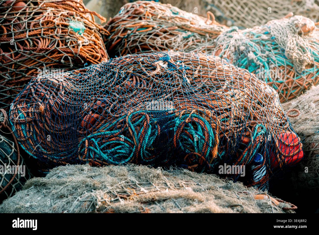 Gros plan d'une pile de filets de pêche dans un port, montrant des filets de pêche enchevêtrés, des cordes et des flotteurs empilés sur le quai, mettant en évidence les textures de l'industrie maritime A. Banque D'Images