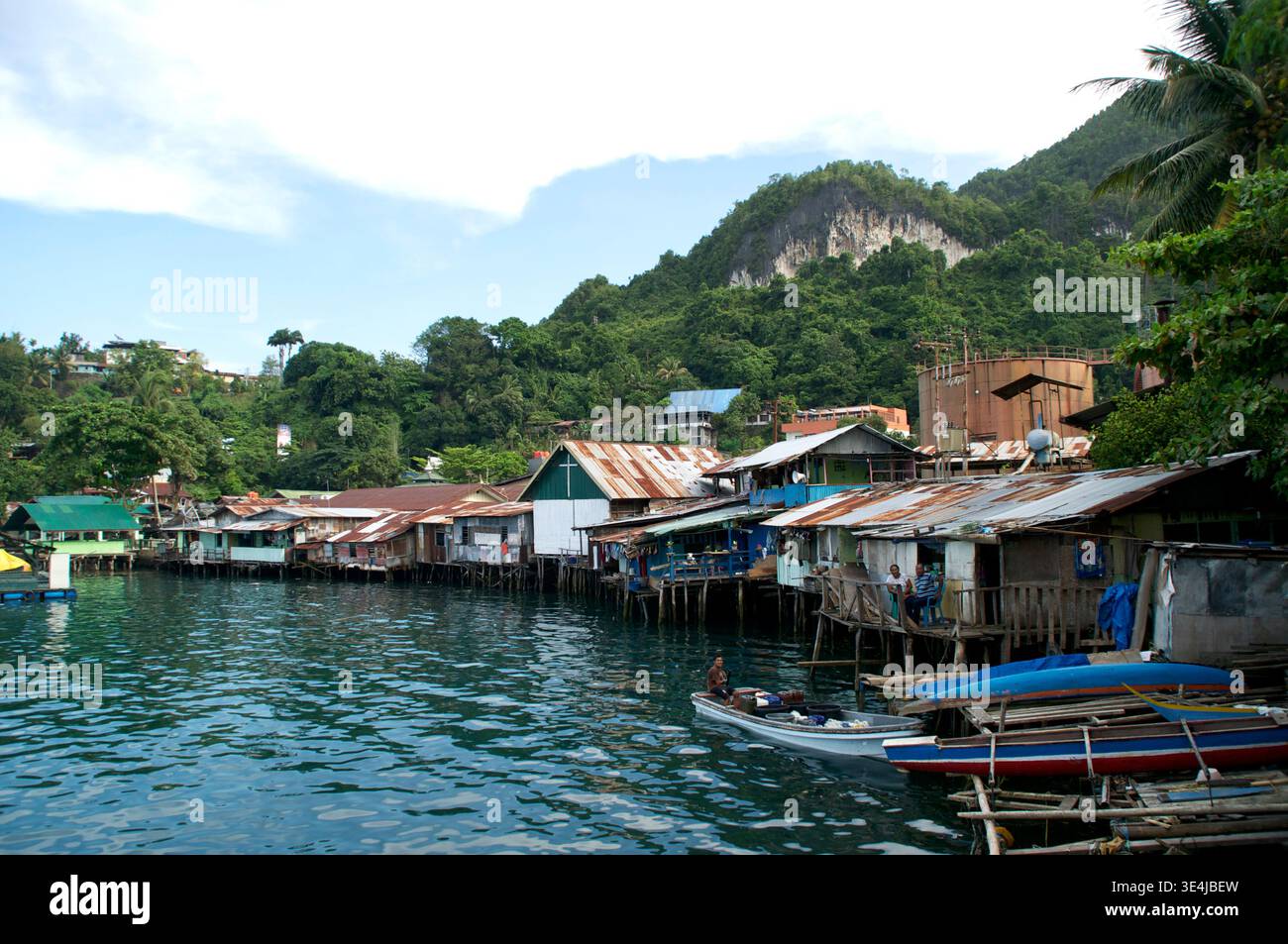 Les maisons sur pilotis bordent le front de mer à Jayapura, Papouasie, Indonésie, avec de petits bateaux et des collines verdoyantes, montrant la vie quotidienne dans la communauté de pêcheurs côtiers. Banque D'Images