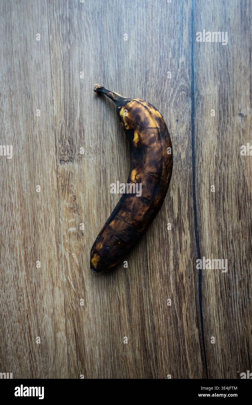 Banane surmûre avec des taches sombres sur la surface en bois, illustrant le gaspillage alimentaire, la détérioration et la pourriture naturelle dans une scène de nature morte minimale Banque D'Images