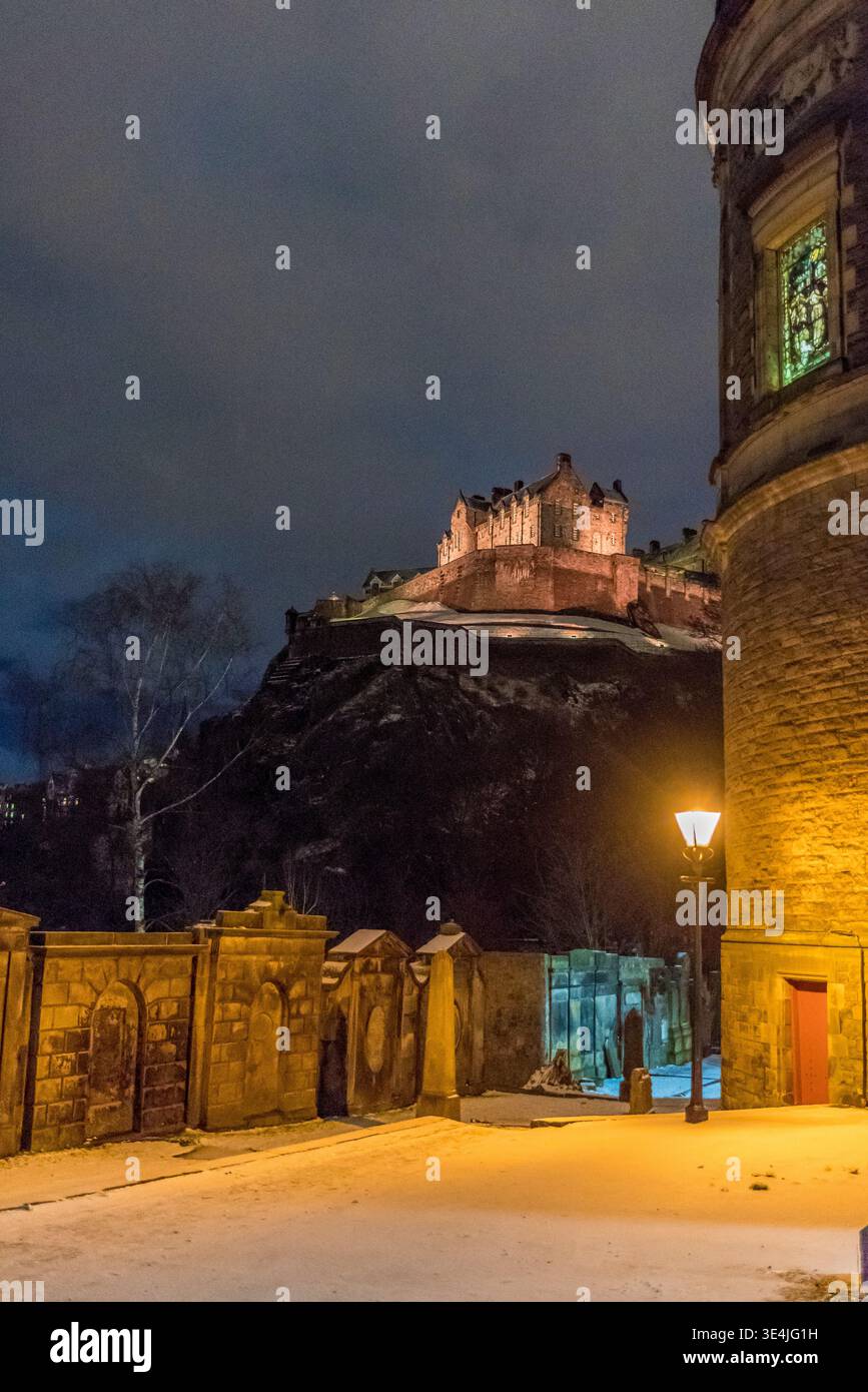 Une vue nocturne sombre du château d'Édimbourg perché sur une falaise rocheuse, photographié depuis le cimetière de St John avec un lampadaire chaud, enneigé gr Banque D'Images