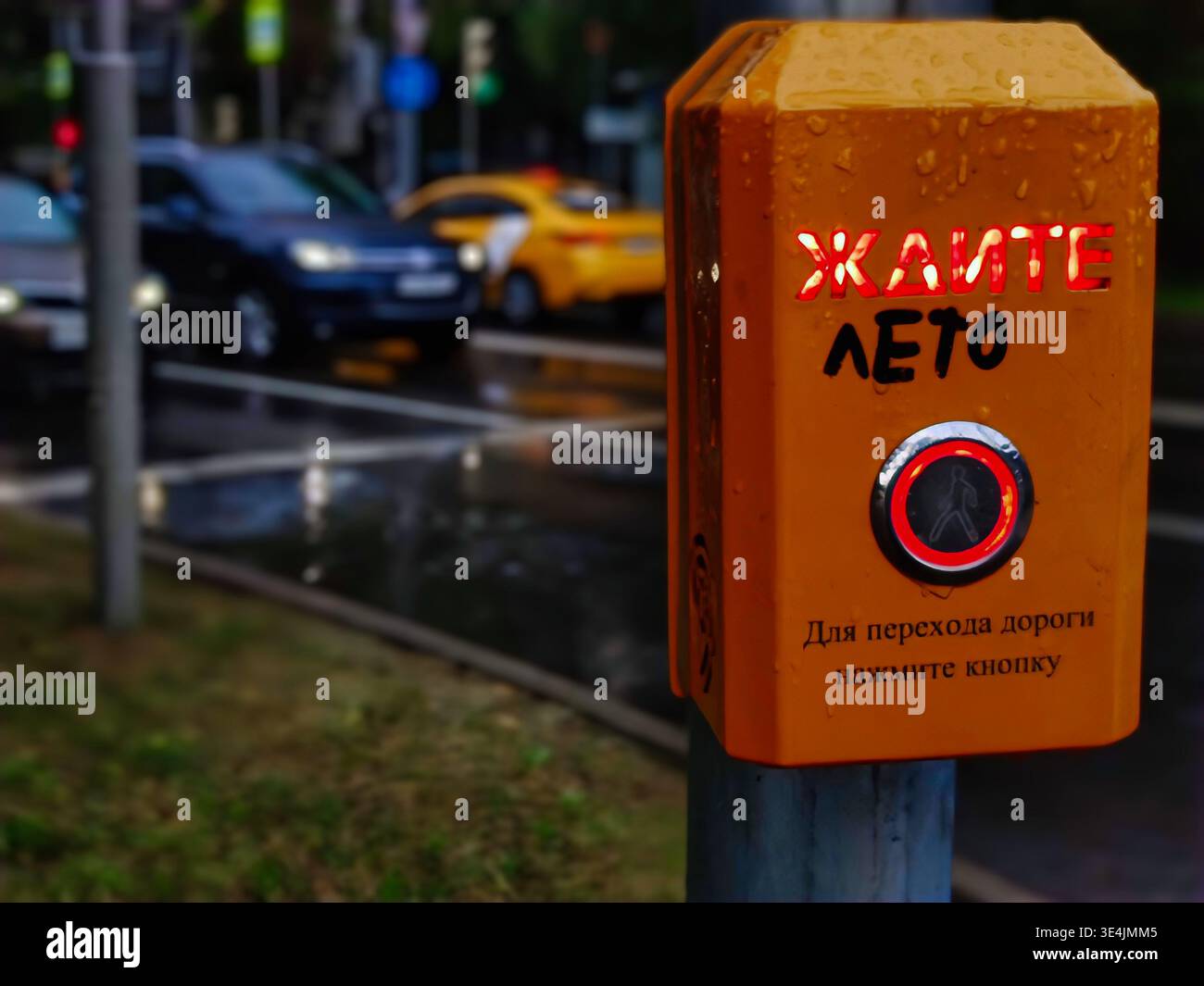 Gros plan d'un bouton de feu de circulation jaune portant le mot rouge « WAIT » et un graffiti manuscrit qui change le sens de « WAIT » Banque D'Images
