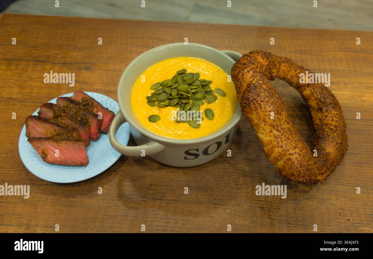 Une photo à grand angle d'un repas copieux avec un bol de soupe crémeuse à la citrouille garnie de graines vertes. Servi avec des tranches juteuses de boeuf moyennement rare Banque D'Images