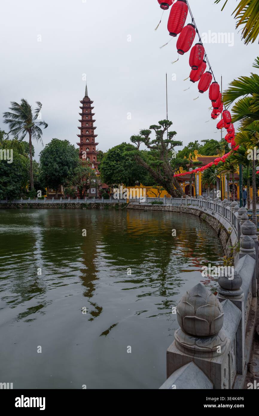 HANOI, VIETNAM – 22 JANVIER 2024 : les visiteurs marchent le long de la passerelle au bord du lac près de la pagode Tran Quoc décorée de lanternes rouges au lac de l'Ouest. Banque D'Images