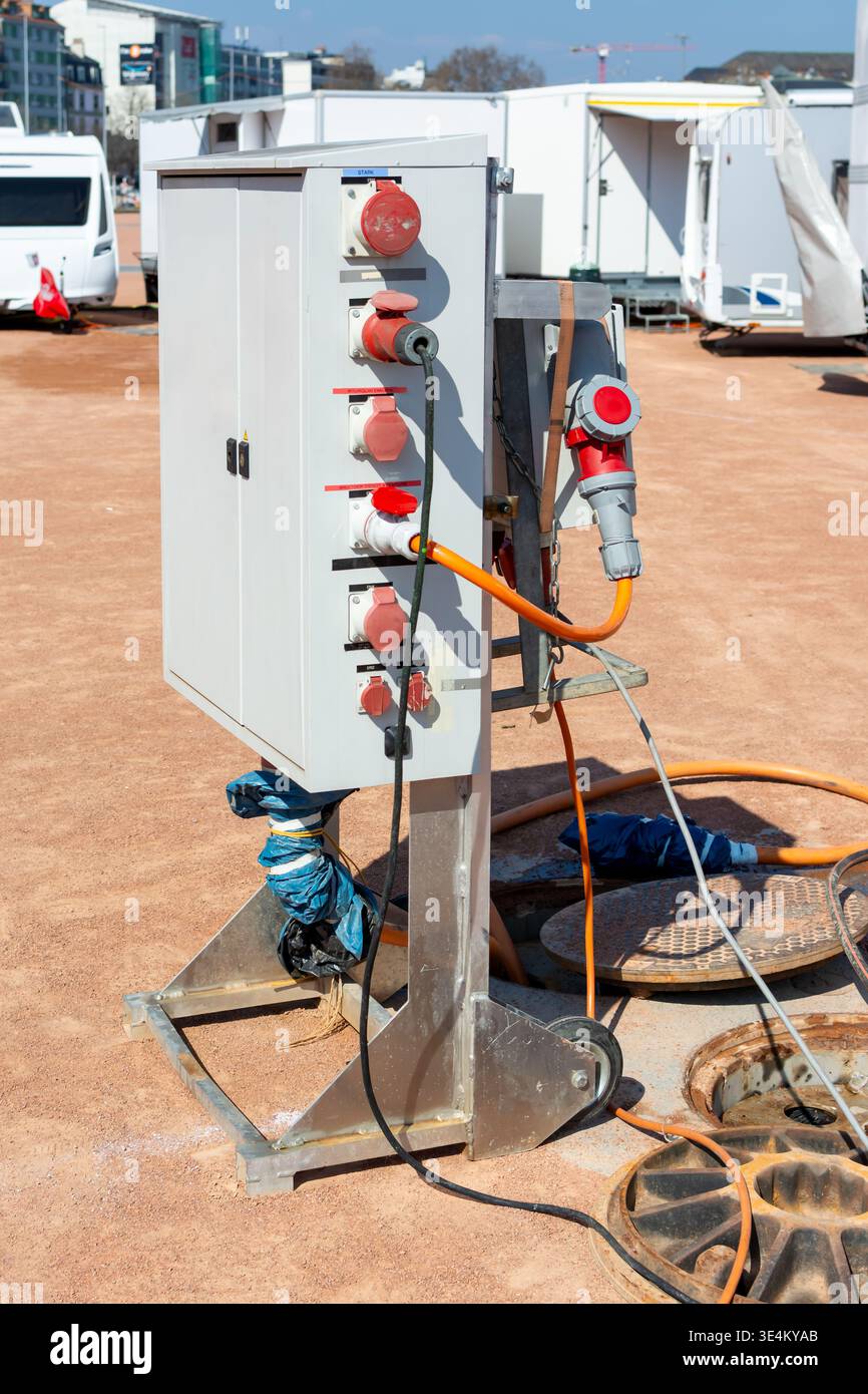 Armoire de raccordement électrique avec prises industrielles et câble orange connecté à côté de fosses ouvertes dans une zone de service temporaire pour caravanes et tr Banque D'Images