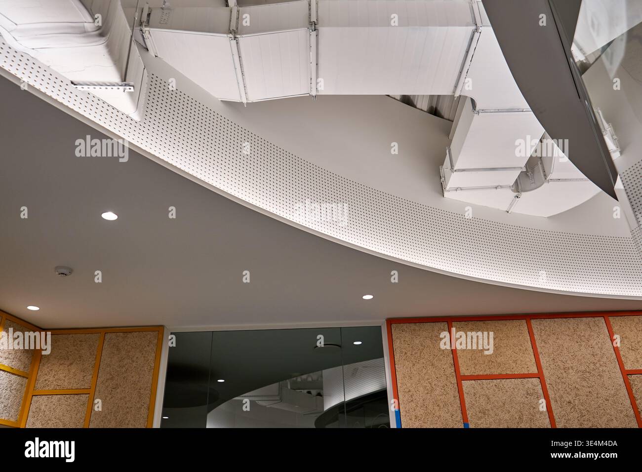 Vue en angle bas d'un plafond intérieur de bureau contemporain avec gaines HVAC blanches apparentes et systèmes de ventilation montés sur blanc incurvé Banque D'Images