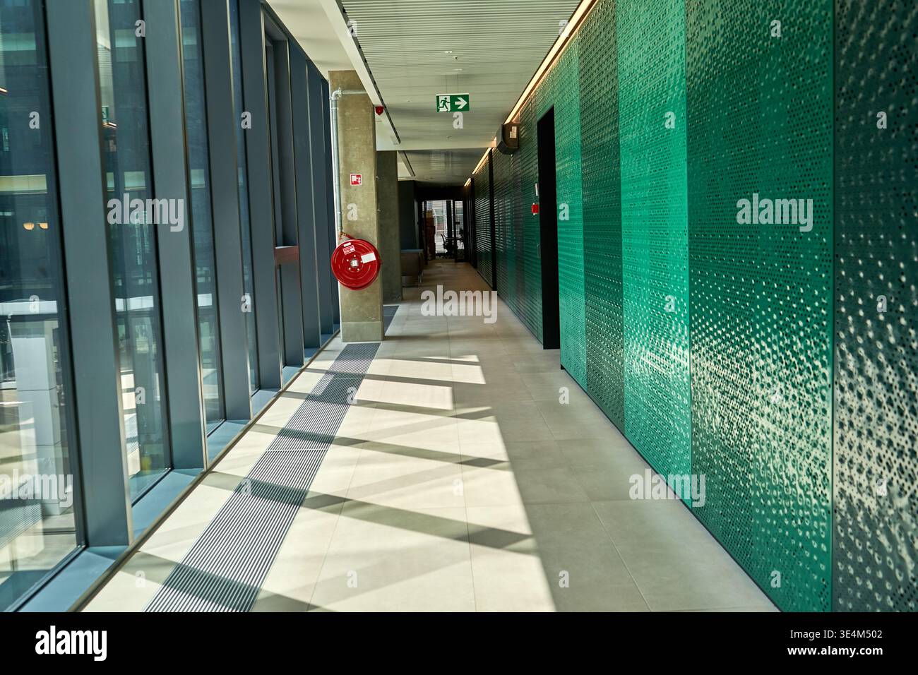 Un couloir moderne et vide dans un immeuble de bureaux contemporain ou un établissement public, avec un mur texturé vert vibrant sur le côté droit avec un Banque D'Images