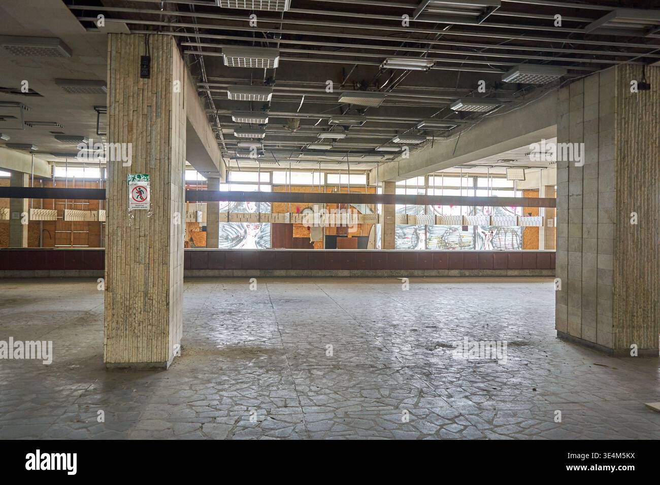 Intérieur d'un grand bâtiment commercial abandonné ou vacant présentant des piliers en béton exposés avec des stries verticales, des planchers fissurés et un Banque D'Images
