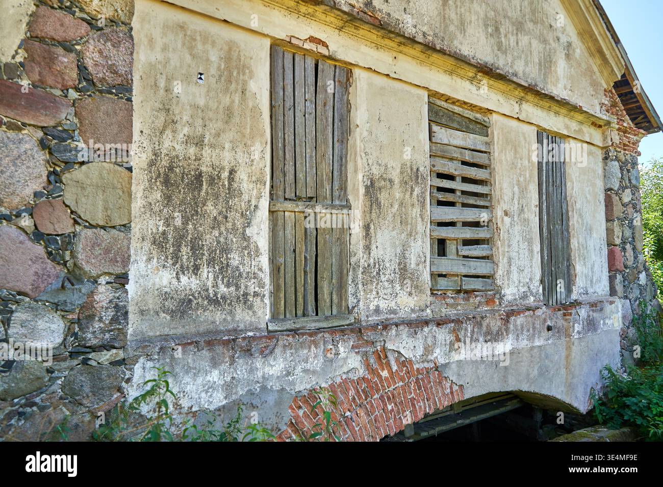 Mur extérieur altéré d'un ancien bâtiment abandonné présentant des matériaux de construction mixtes, y compris de la maçonnerie en pierre irrégulière, des briques rouges, et Banque D'Images