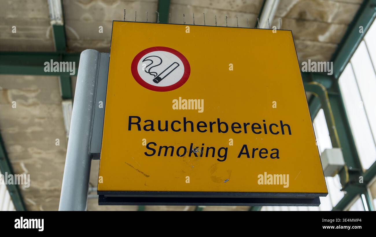 Panneau jaune zone fumeurs dans une zone d'attente ferroviaire, indiquant clairement un espace réservé aux fumeurs dans un environnement de transport public. Banque D'Images
