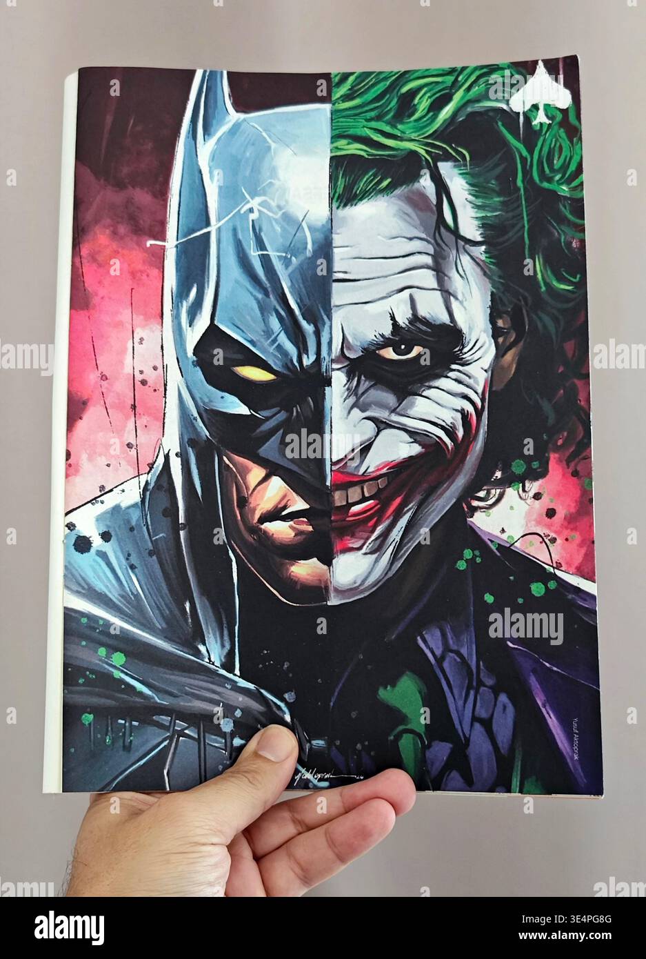 Main tenant un magazine turc présentant une illustration artistique à visage fendu du du Joker de Batman et Heath Ledger, stylisée comme une carte à jouer à pique. Banque D'Images