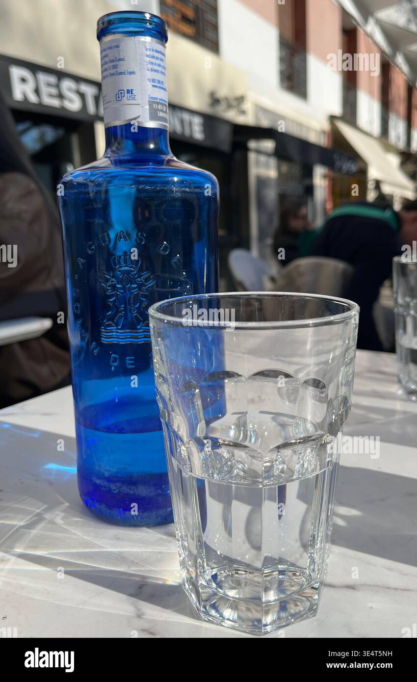 Bouteille en verre bleu de Solan de Cabras Minteral eau d'un spa à Cuenca avec un verre clair sur une table de terrasse au soleil Madrid Espagne Europe - Image de stock capturée avec un smartphone