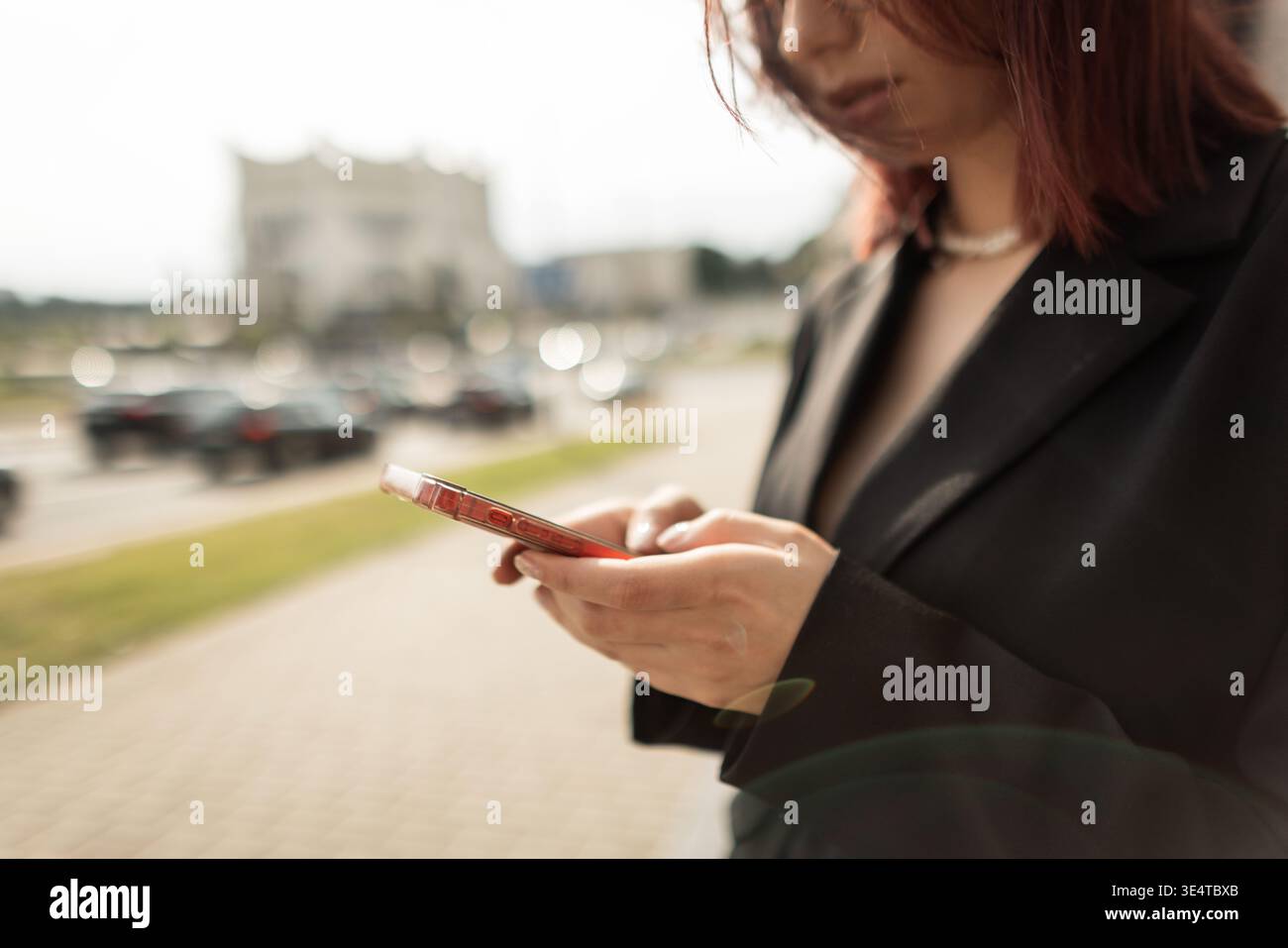 Femme aux cheveux roux confiante utilisant un téléphone portable à l'extérieur. Look élégant, vibes de ville, journée ensoleillée, concept de technologie et de communication. Jeune femme adulte f Banque D'Images