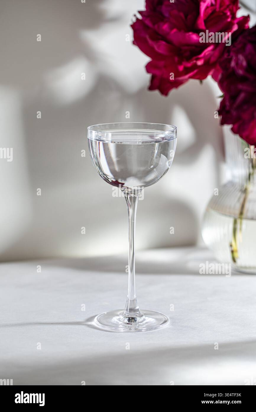 Verre à cocktail clair avec des fleurs dans une lumière douce Banque D'Images