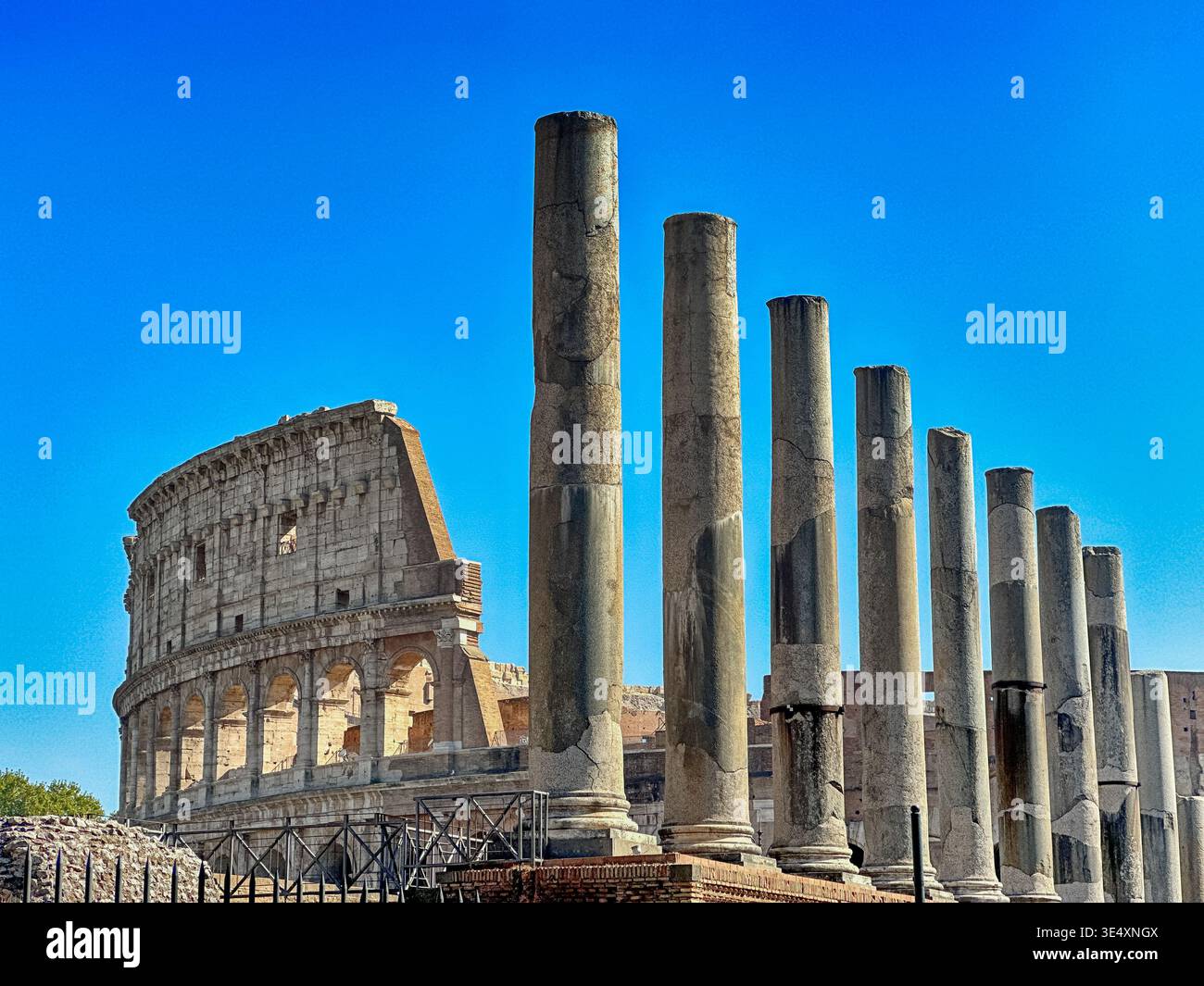 Une rangée d'anciennes colonnes de pierre près d'une entrée du Forum romain se dresse devant les ruines du Colisée romain. Banque D'Images