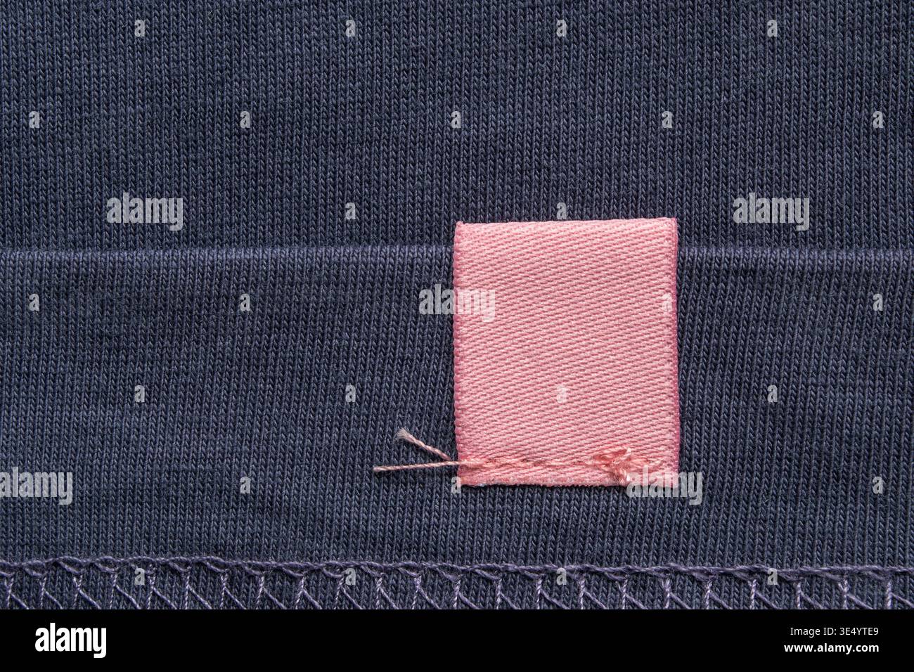 Étiquette de tissu rose vierge cousue sur fond de tissu bleu foncé gros plan Banque D'Images