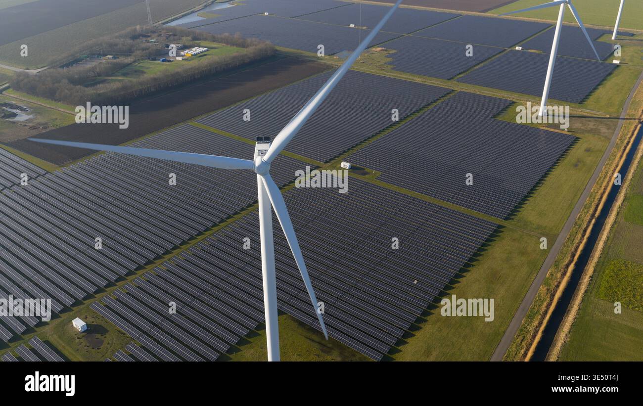 Vue aérienne d'une vaste ferme solaire et d'éoliennes générant de l'énergie propre à travers des champs verts sous un ciel dégagé. Banque D'Images