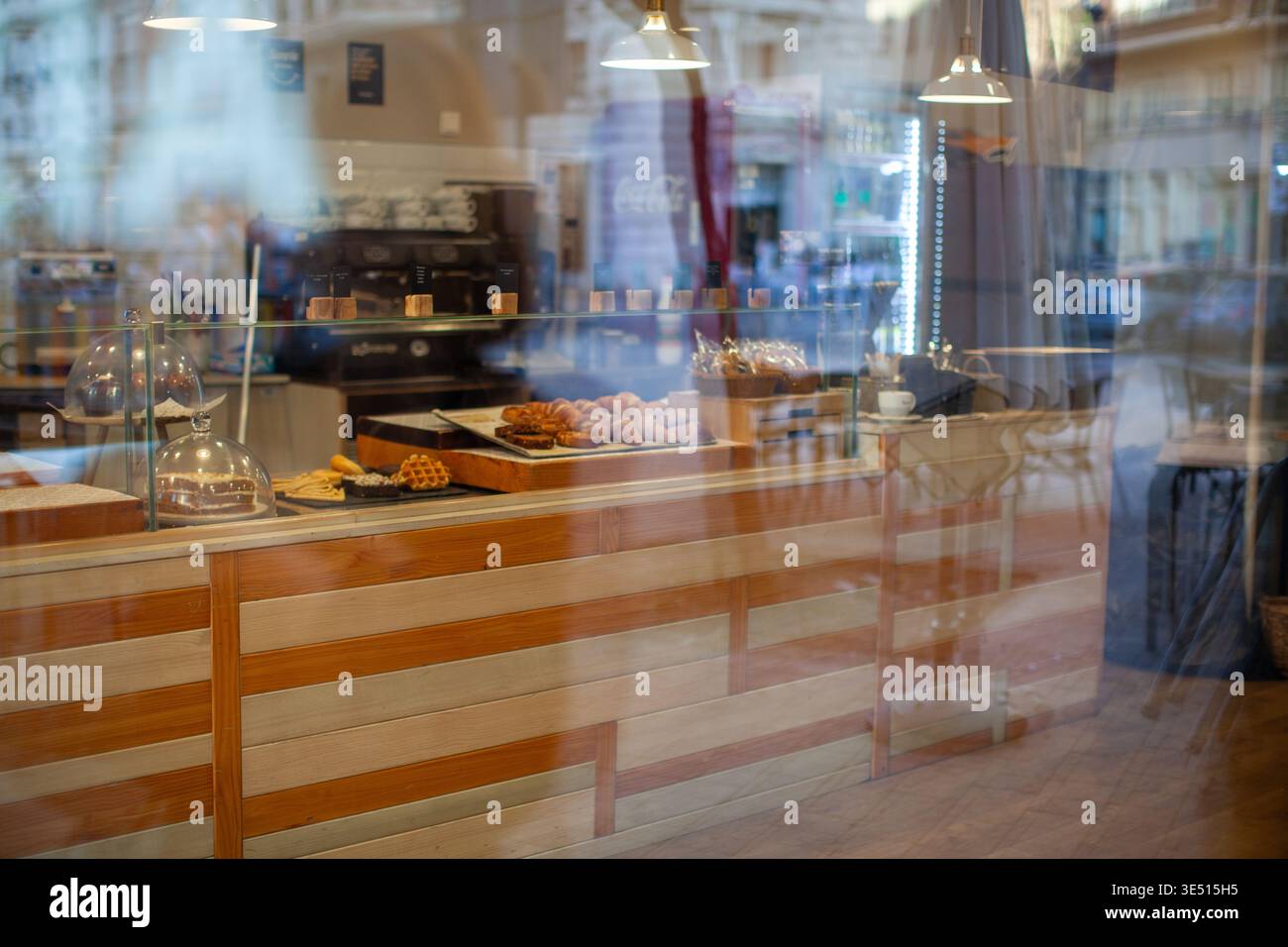 Vitrine de boulangerie avec pâtisseries et desserts assortis visible à travers la vitre, comptoir en bois et machine à café en arrière-plan, invitant Banque D'Images