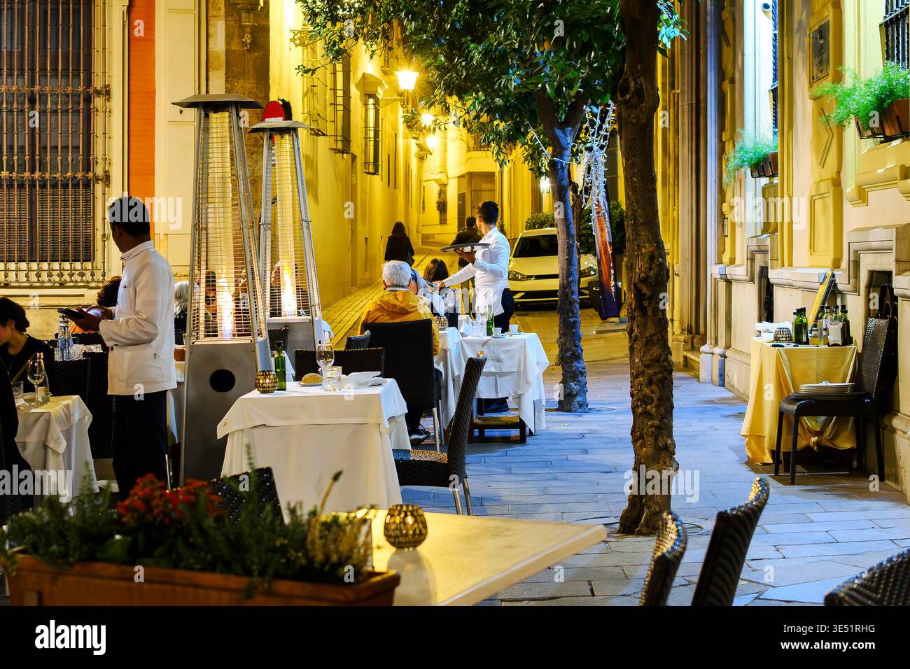 Un café élégant et éclairé sur le trottoir dans une ruelle pittoresque dans le quartier historique de Barrio Santa Cruz à Séville, en Espagne, la nuit. Banque D'Images