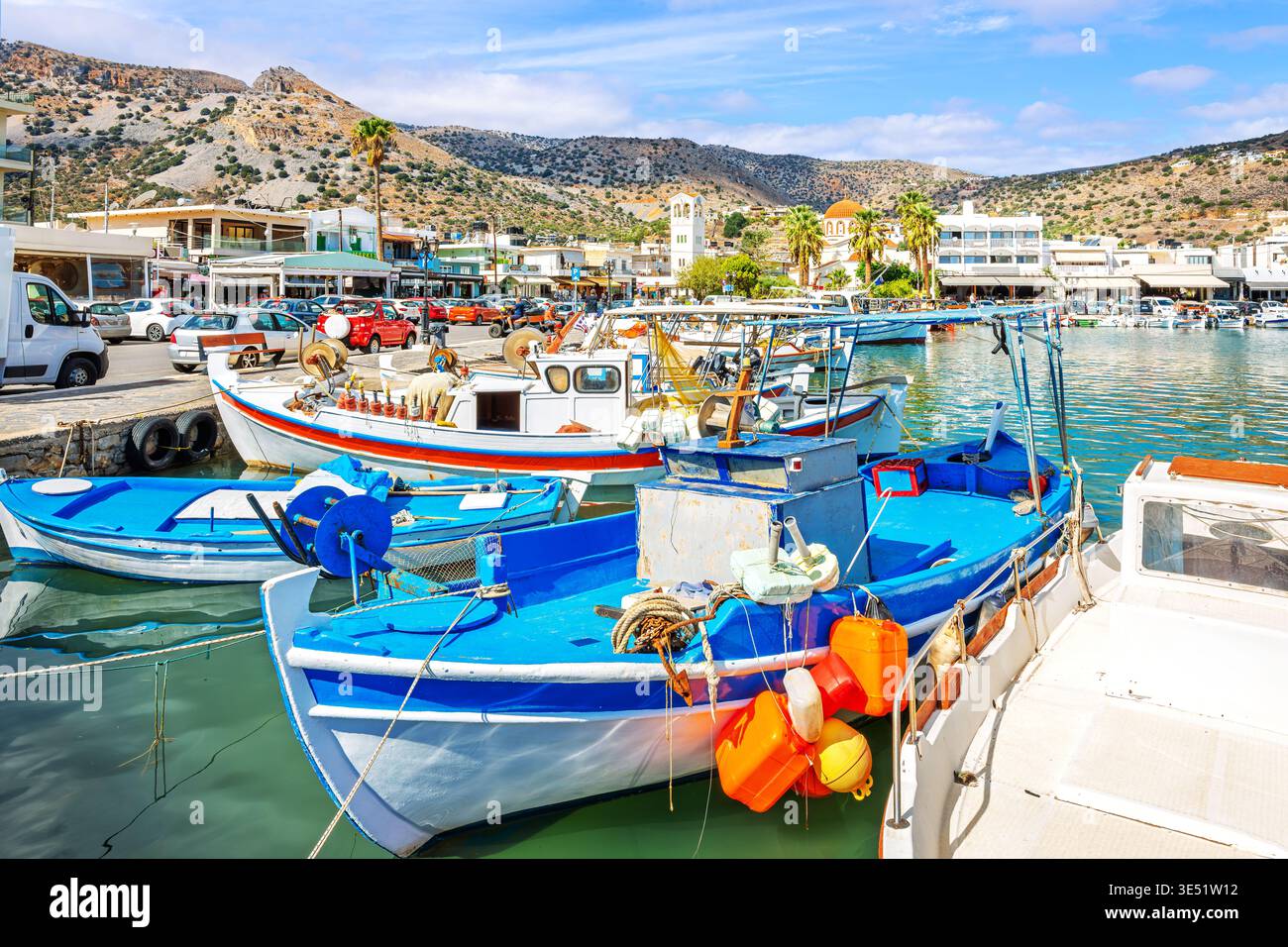 Des bateaux de pêche colorés bordent la marina avec la ville pittoresque et les montagnes derrière dans la ville grecque balnéaire d'Elounda, Grèce, île de Crète. Banque D'Images