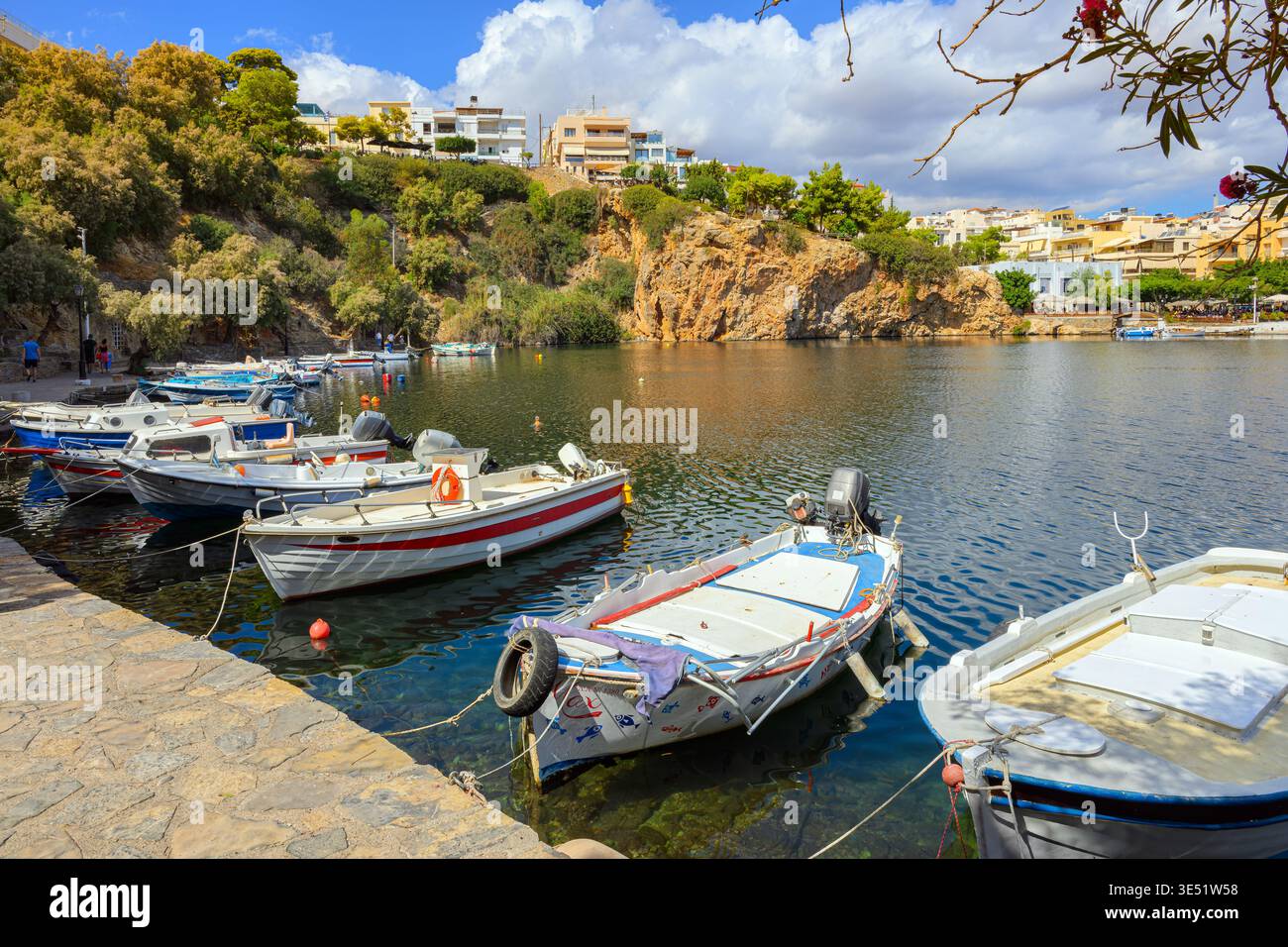 Bateaux de pêche grecs amarrés le long de la promenade du lac Voulismeni, avec les falaises rocheuses et la vieille ville colorée en arrière-plan, à Agios Nikolaos, Grèce, Crète Banque D'Images
