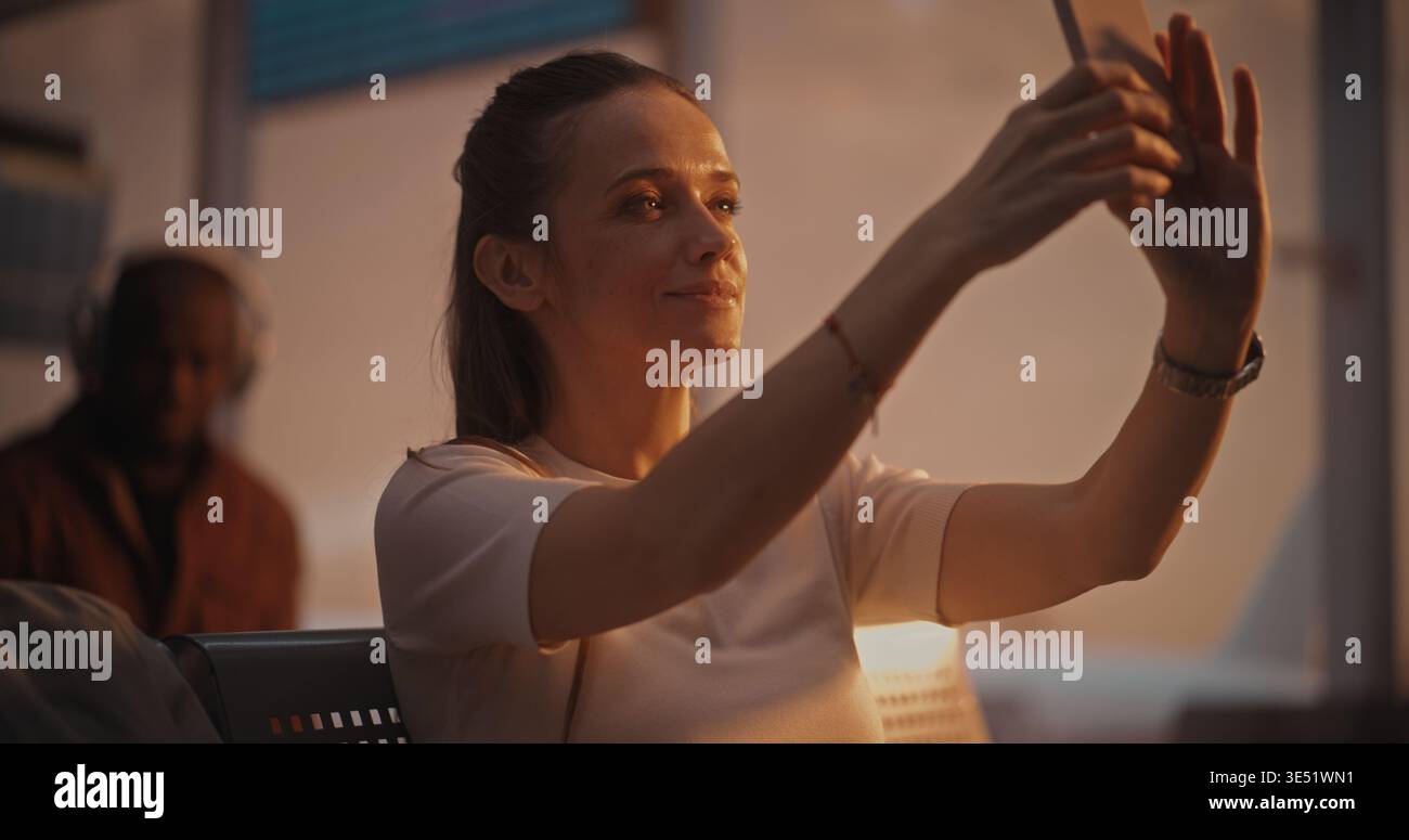 Assise avec la valise près, la femme s'engage dans un appel vidéo pendant l'escale. Femme regarde dans la caméra du téléphone, riant et discutant. Mode de vie des voyageurs connectés. Communications mobiles, connectivité 5G. Banque D'Images