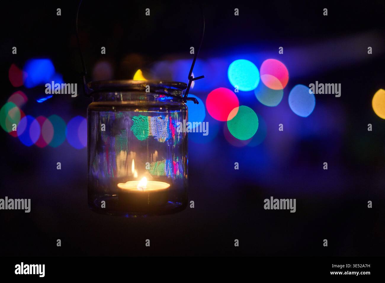 Une photographie rapprochée d'une bougie allumée de bougie de thé brûlant à l'intérieur d'une lanterne de pot en verre transparent avec un couvercle fermoir en métal et une poignée en fil de fer, suspendue dans le Banque D'Images