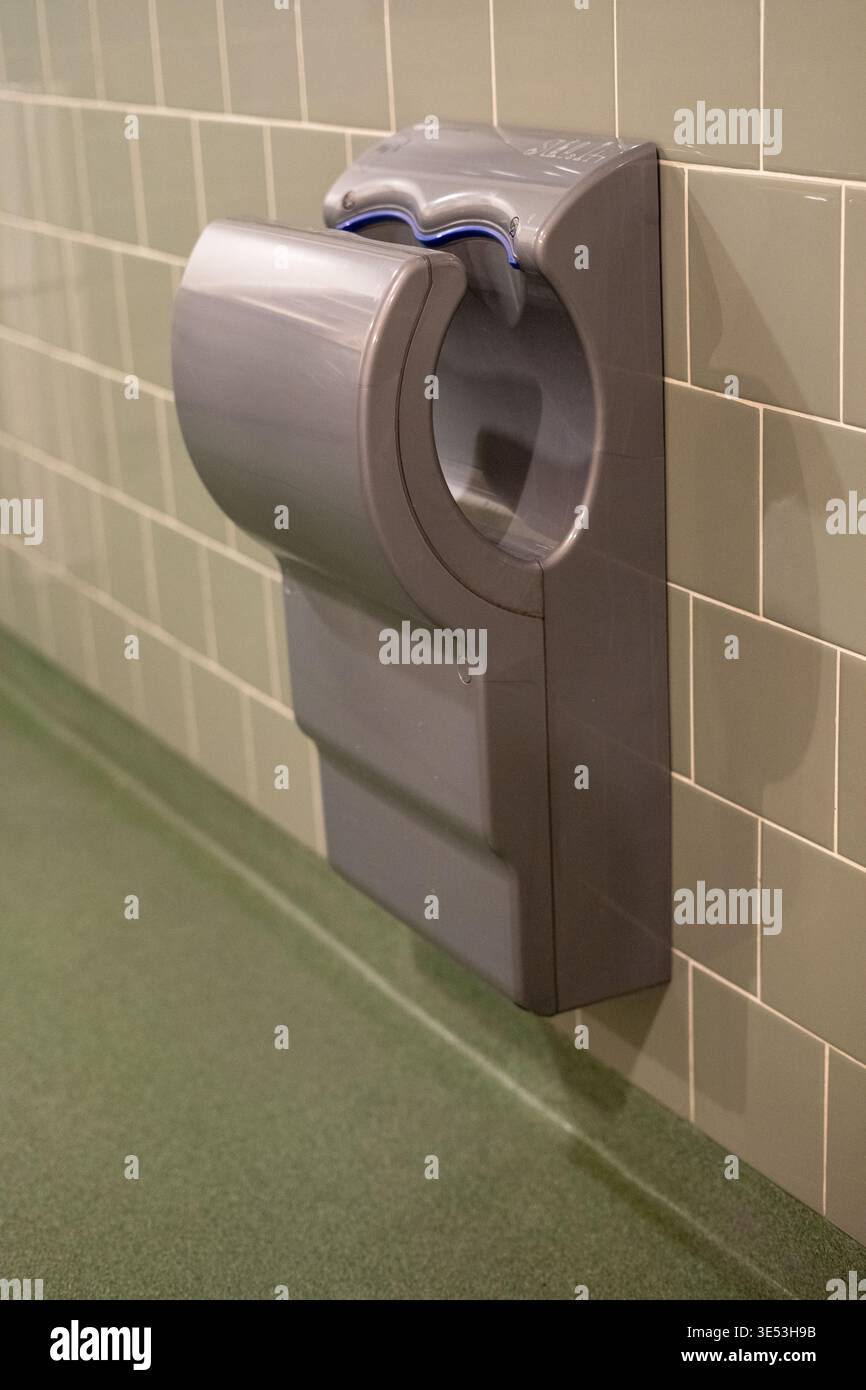 Sèche-mains automatique moderne dans les toilettes publiques. Concept d'hygiène et d'assainissement avec technologie sans contact sur mur carrelé. Banque D'Images