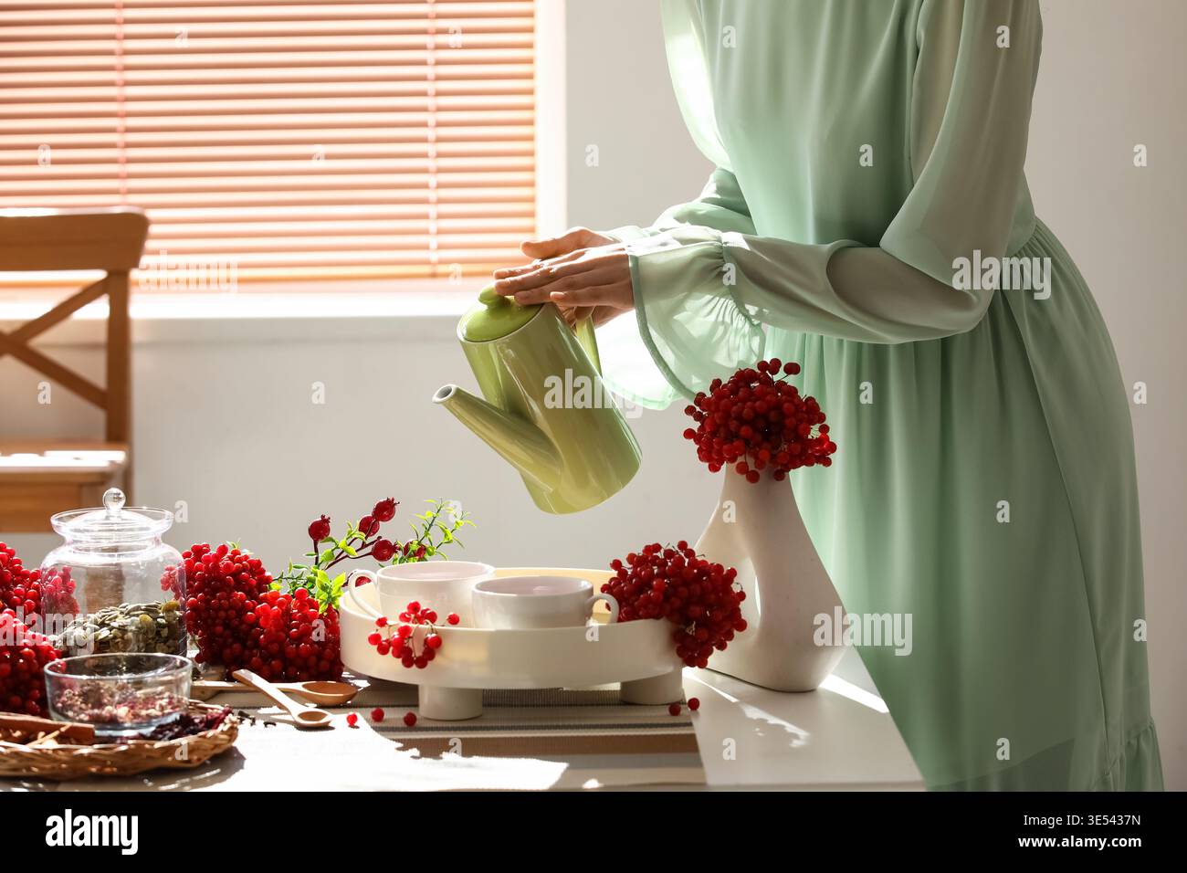 Jeune femme versant du thé viburnum de la théière dans la tasse à la maison Banque D'Images