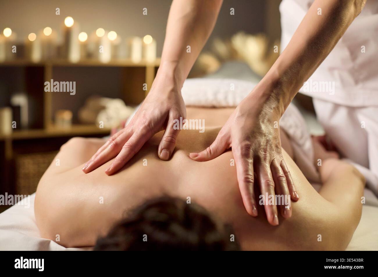 Massage du dos professionnel avec mains apaisantes, bougies et ambiance calme Banque D'Images