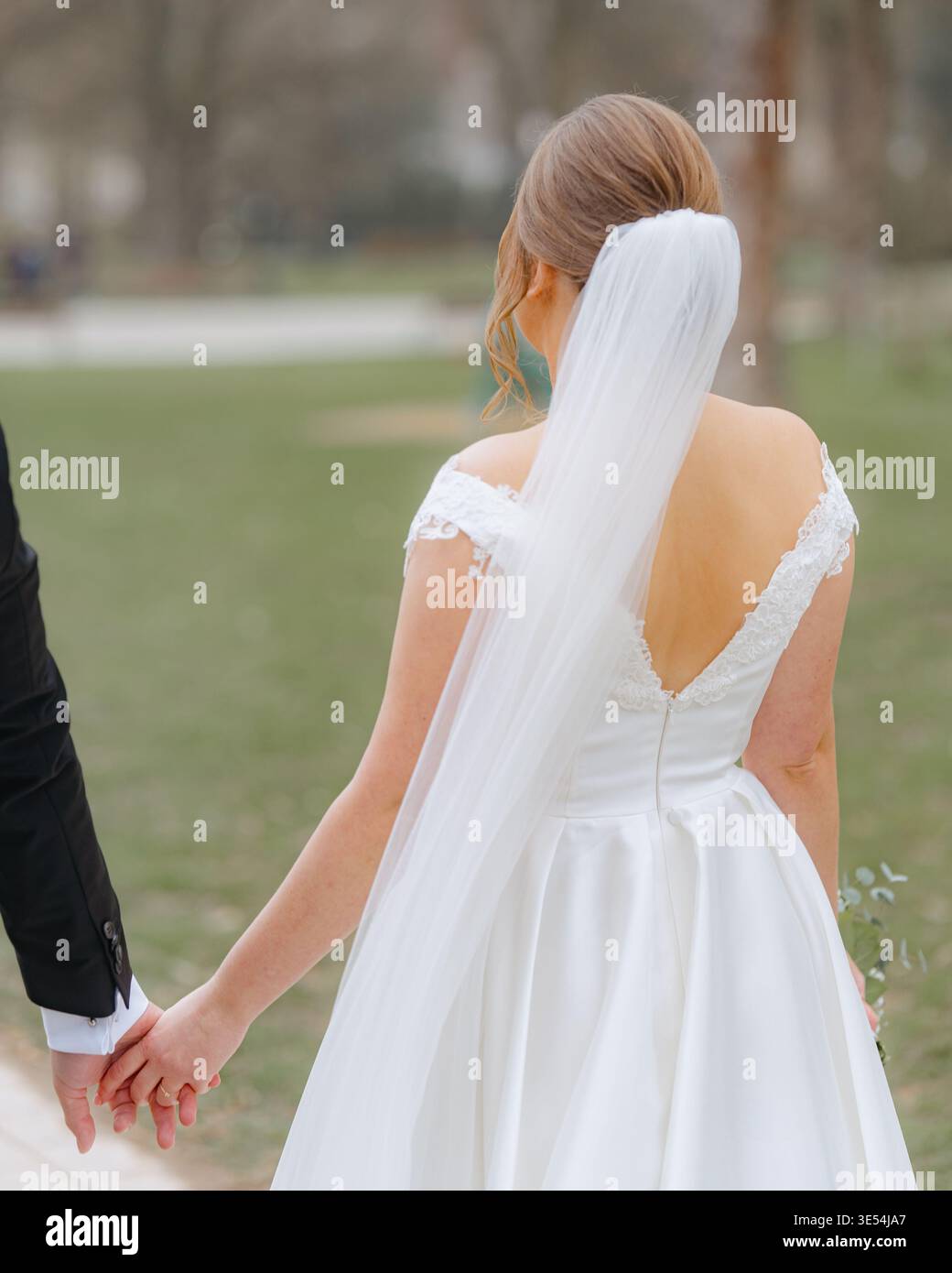Couple de mariage marchant ensemble par derrière dans un parc. Moment romantique d'amour, d'unité et de nouveau commencement. Scène de mariage extérieure naturelle. Banque D'Images