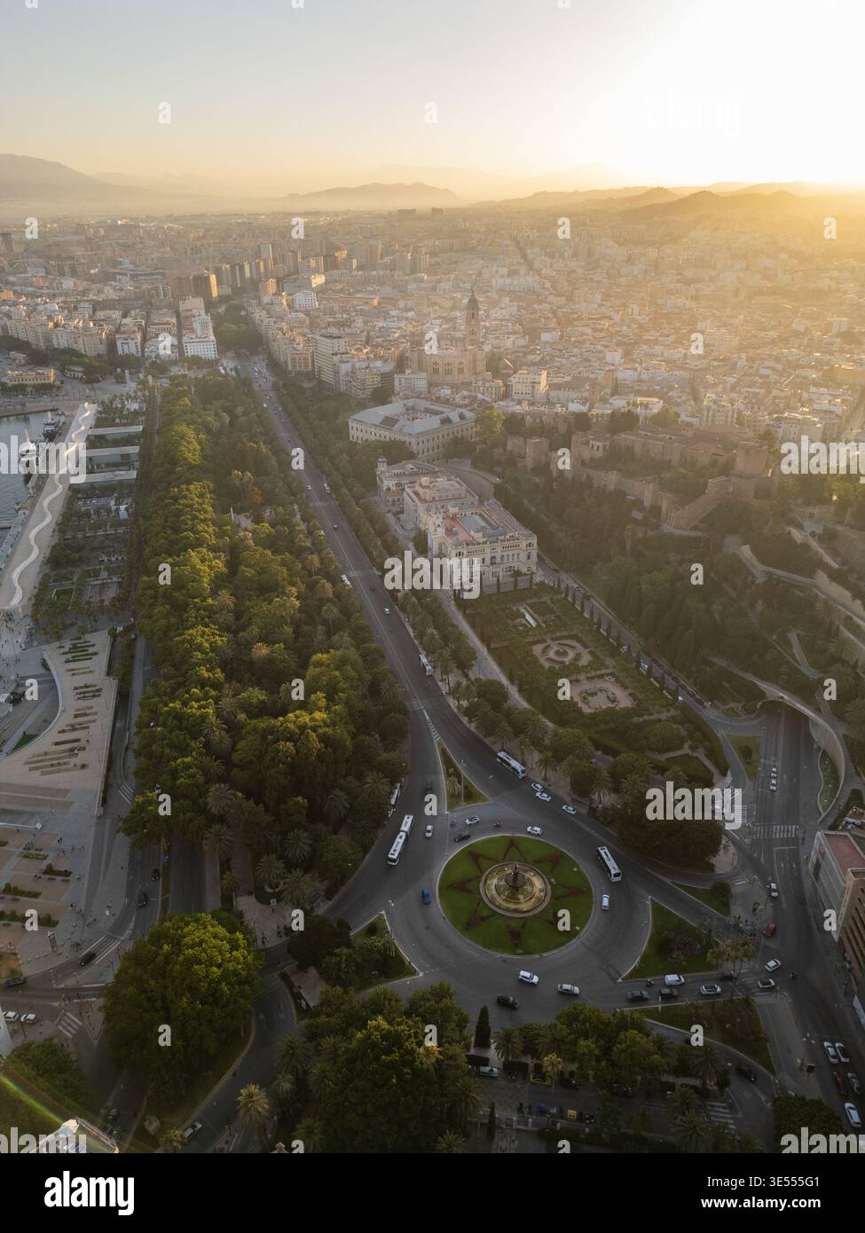 Vue aérienne sur le parc luxuriant de la ville, l'historique Alcazaba, et un rond-point central pendant un coucher de soleil doré à Malaga, Andalousie, Espagne. Banque D'Images