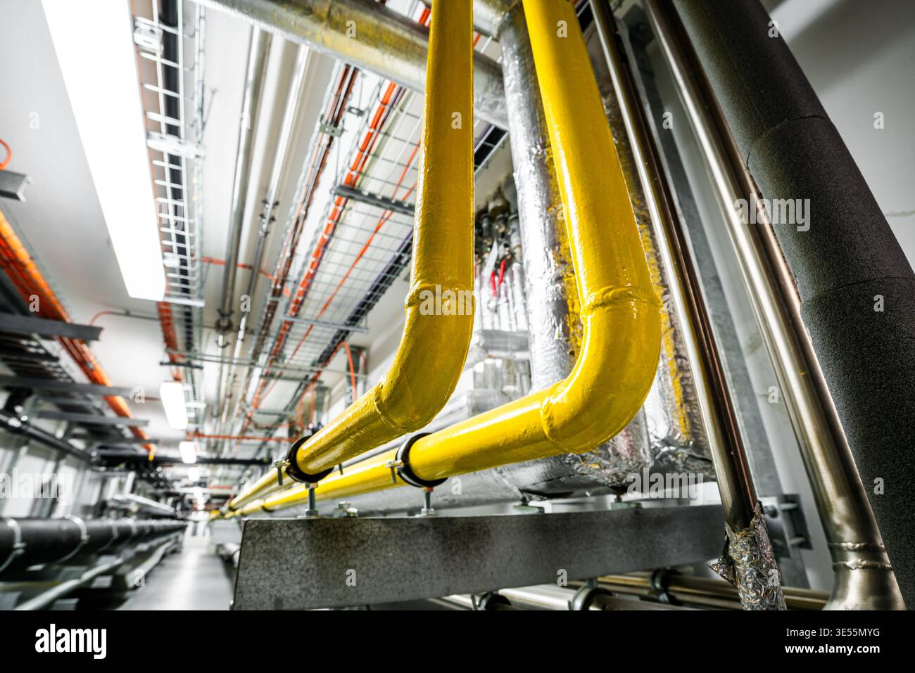 Vue à angle réduit d'une installation HVAC avec des gazoducs jaunes le long de conduits isolés et de chemins de câbles. Banque D'Images