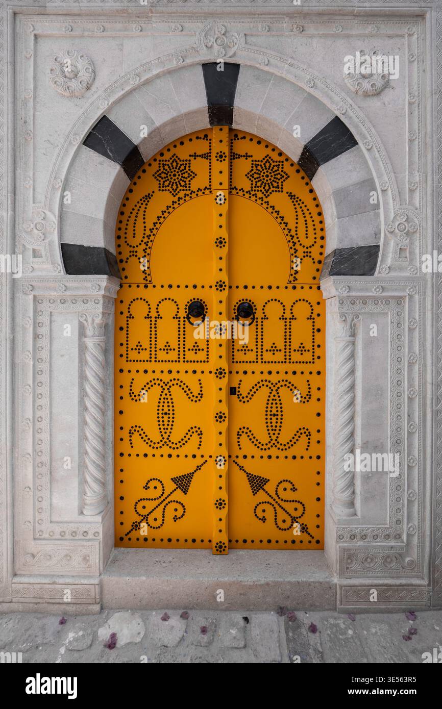 Vue d'une porte traditionnelle jaune cloutée avec des motifs noirs complexes et une arche en pierre sculptée à Tunis, Gouvernorat de Tunis, Tunisie. Banque D'Images
