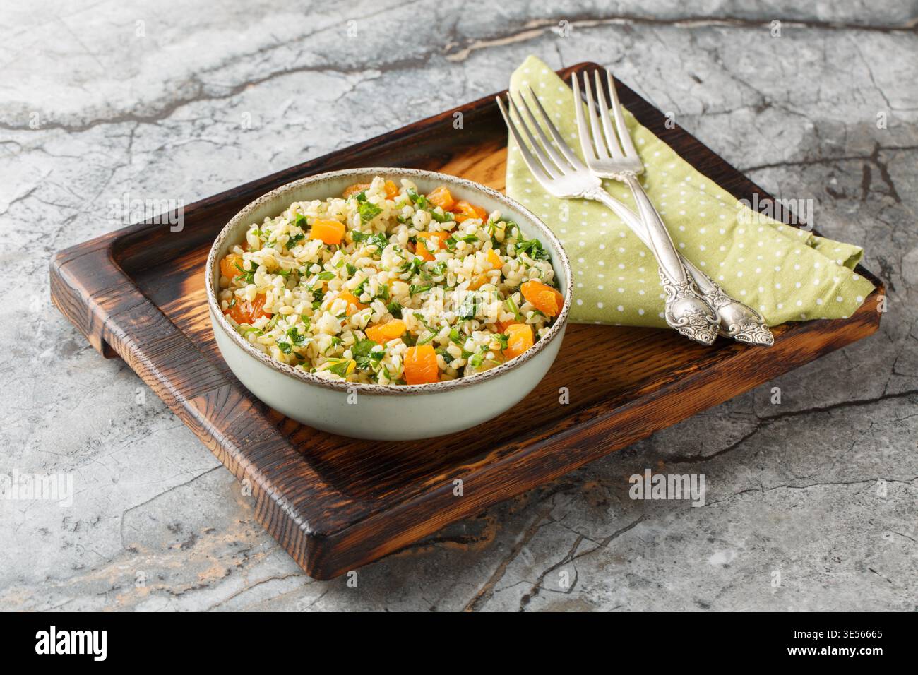 Bulgur cuit à la vapeur avec persil, abricots séchés et huile d'olive gros plan dans un bol sur la table. Horizontal Banque D'Images